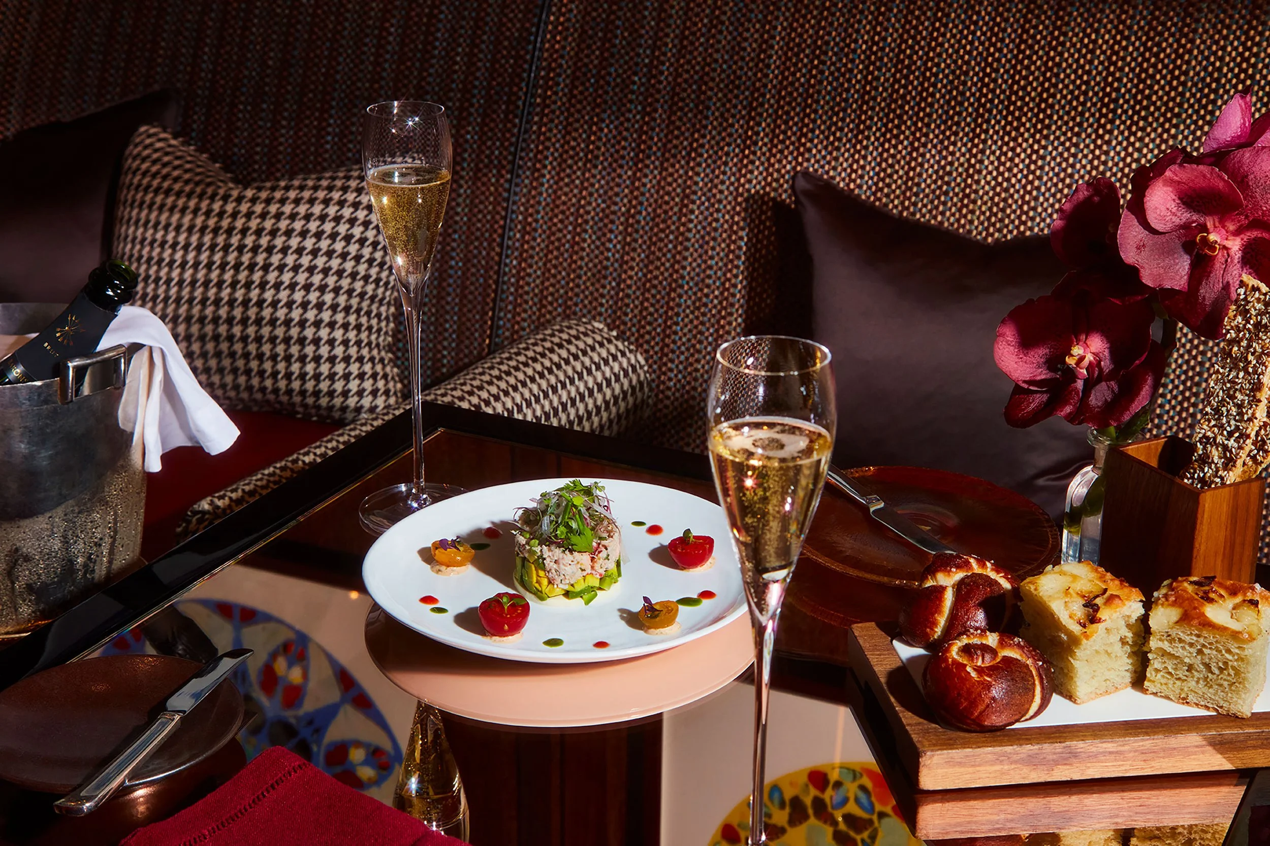 Elegant restaurant table with plated gourmet salad, champagne flutes, bread, flowers, and patterned seating.