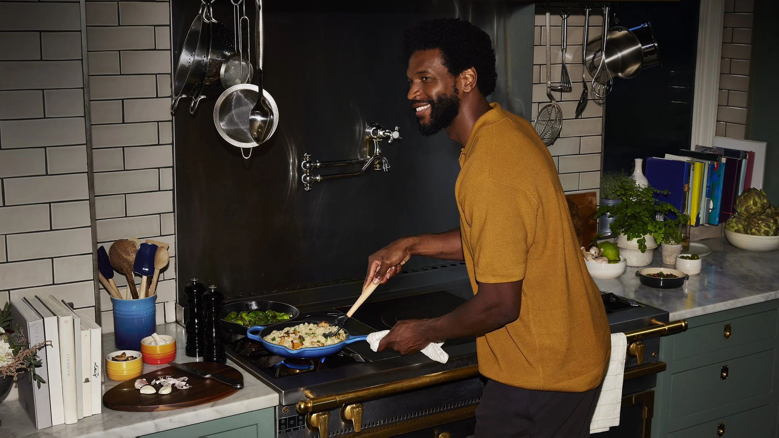 Smiling man cooking creamy rice and green vegetables in a skillet on a professional kitchen stove