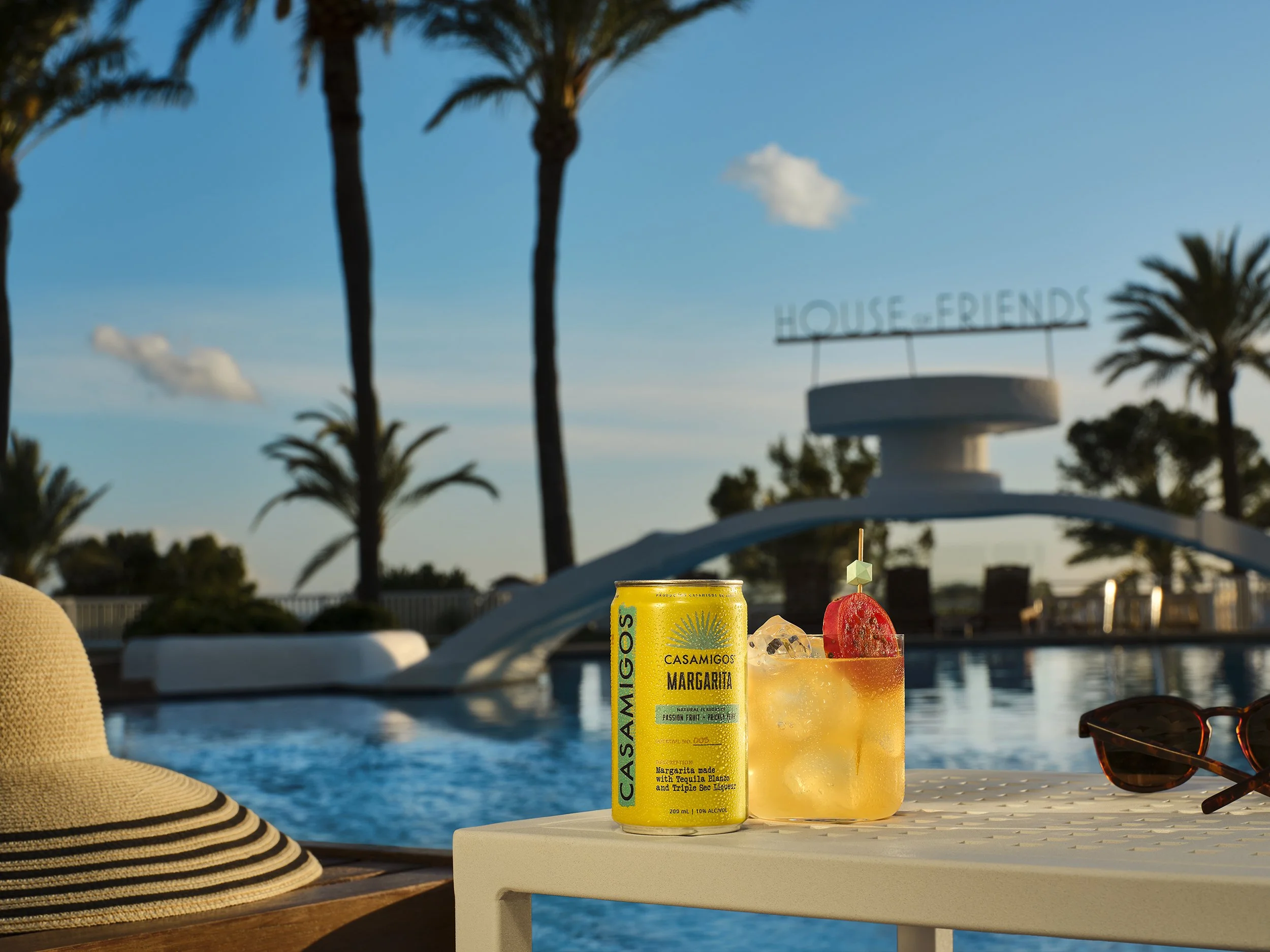 Casamigos Margarita can and passion fruit margarita by a pool with palm trees, sunglasses, and a sun hat