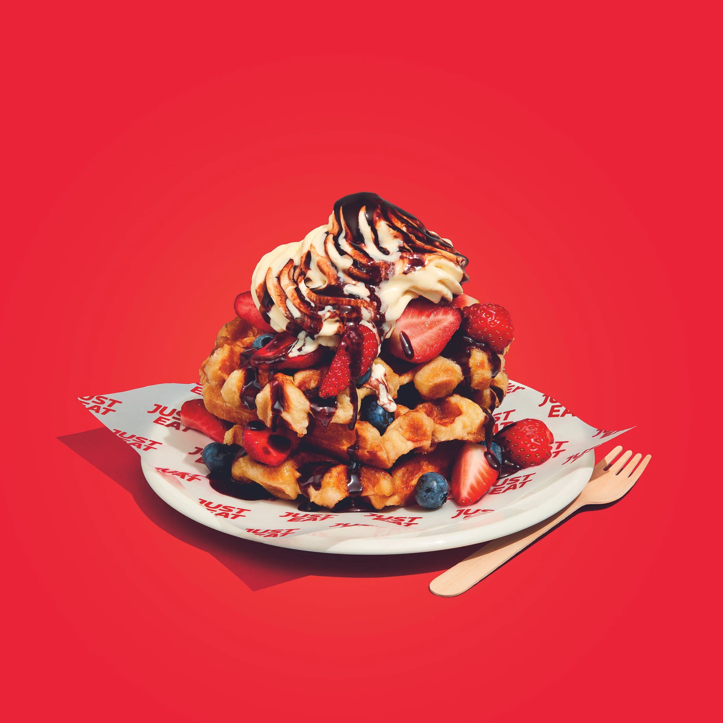 Belgian waffles topped with vanilla ice cream, chocolate sauce, strawberries, and blueberries on a branded plate