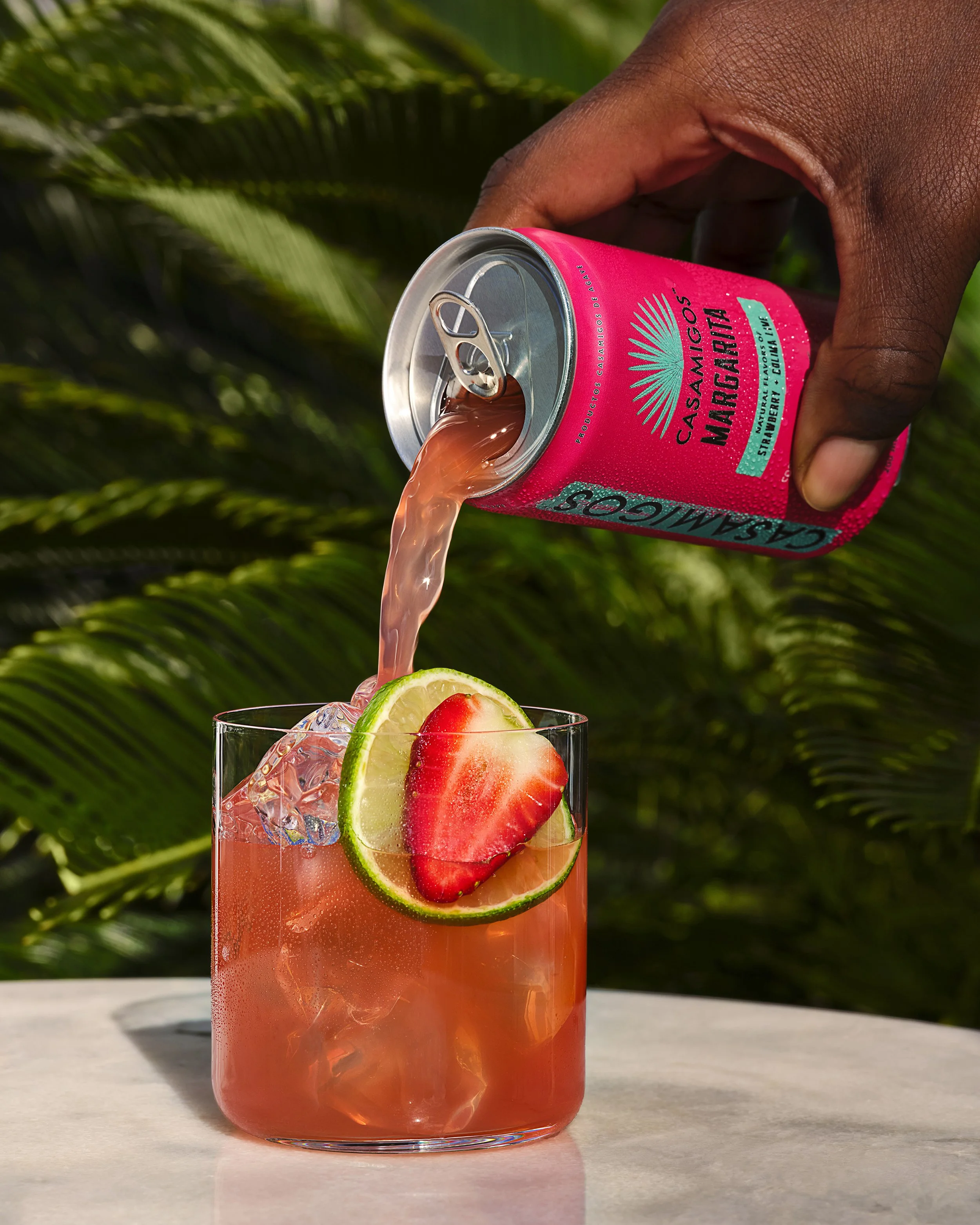 Pink Casamigos margarita can pouring a strawberry-lime cocktail over ice, garnished with lime and strawberry.
