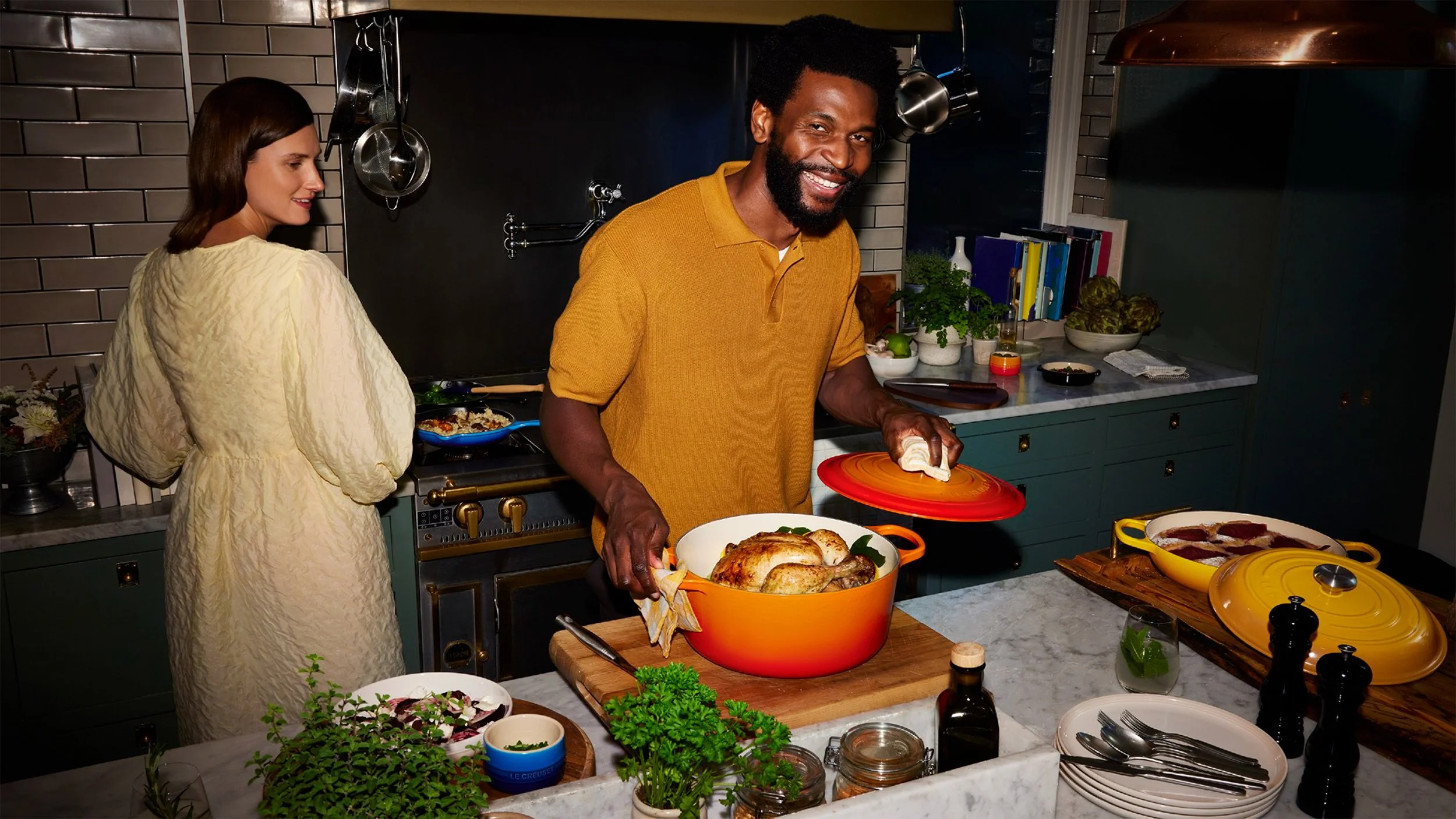 Two people preparing a roast chicken and side dishes in a stylish kitchen