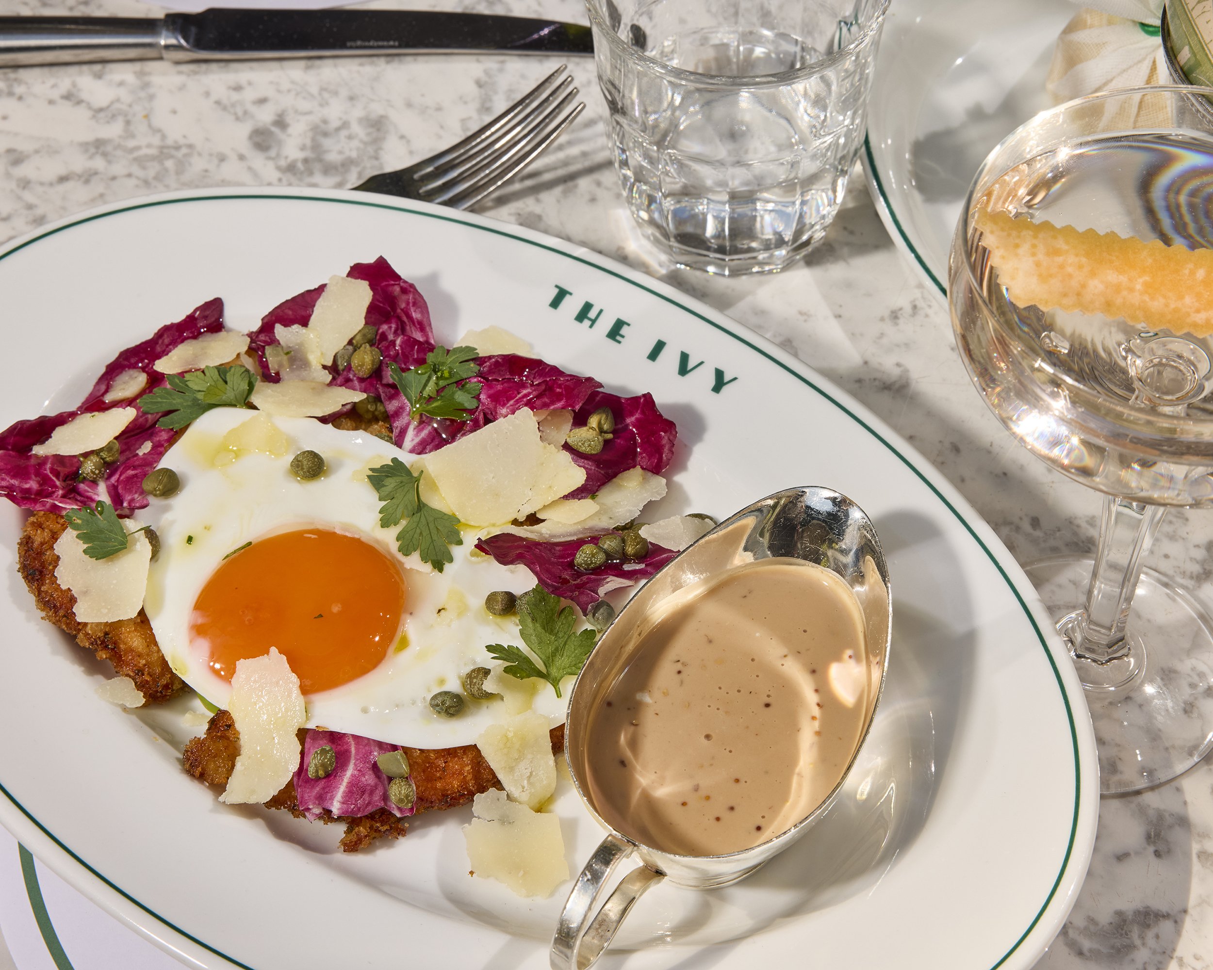 Breaded chicken cutlet topped with a fried egg, radicchio, capers, parsley, and shaved Parmesan, served with creamy sauce