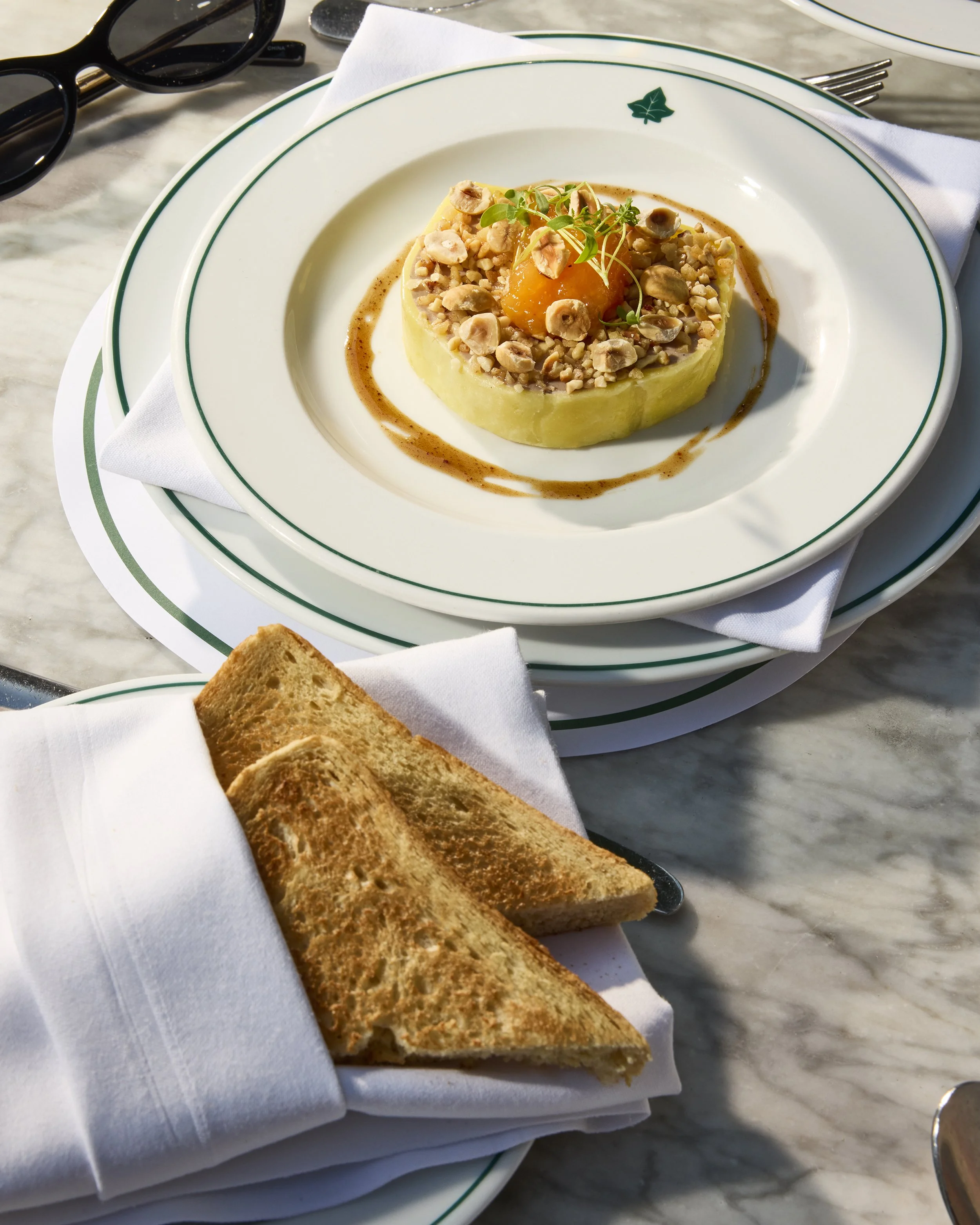 Gourmet plated dish topped with mushrooms, nuts, microgreens, and orange sauce, served with toasted bread at a restaurant table