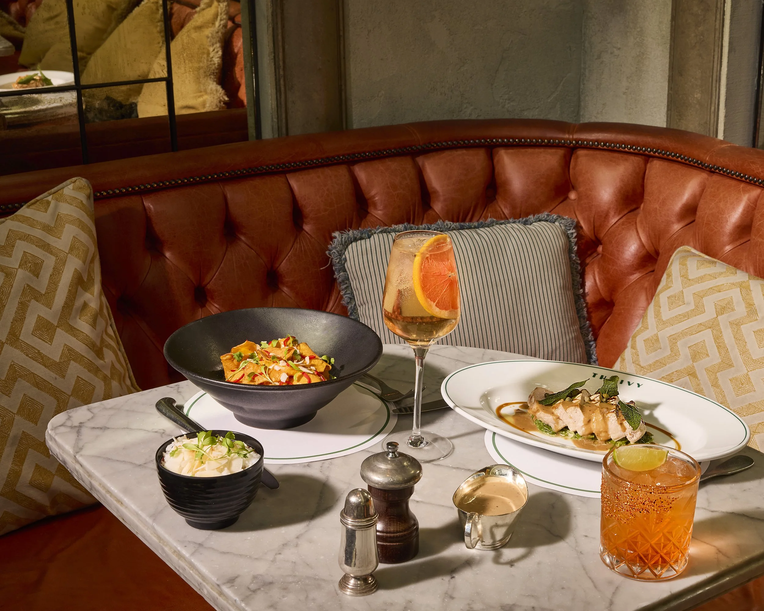 Restaurant table with plated dishes, orange cocktails, and a red leather booth