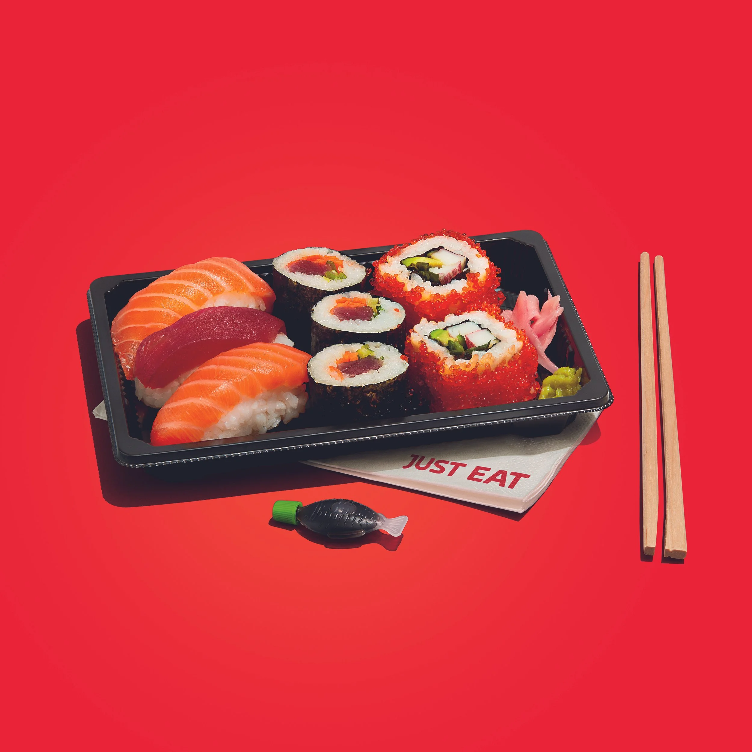 Assorted sushi platter with salmon and tuna nigiri, sushi rolls, pickled ginger, wasabi, chopsticks, and soy sauce on a red background