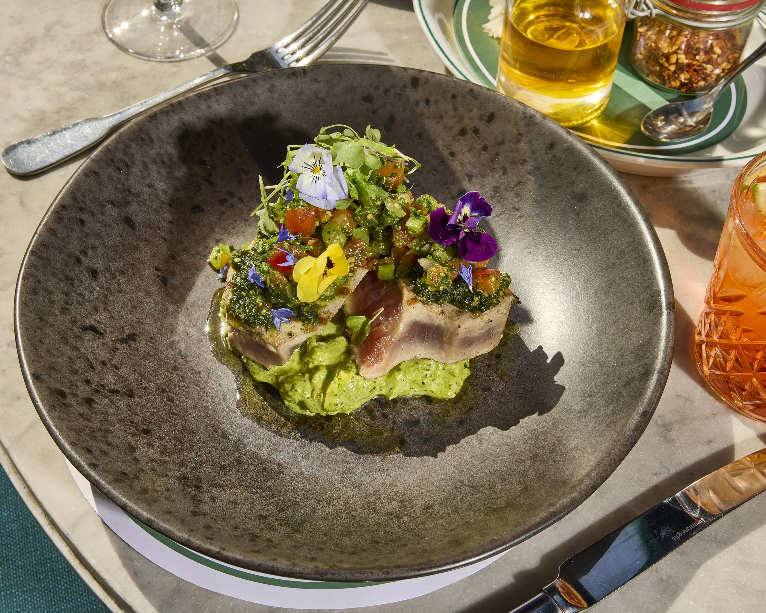 Gourmet fish dish topped with tomato herb salsa and edible flowers on green sauce, served with cocktails