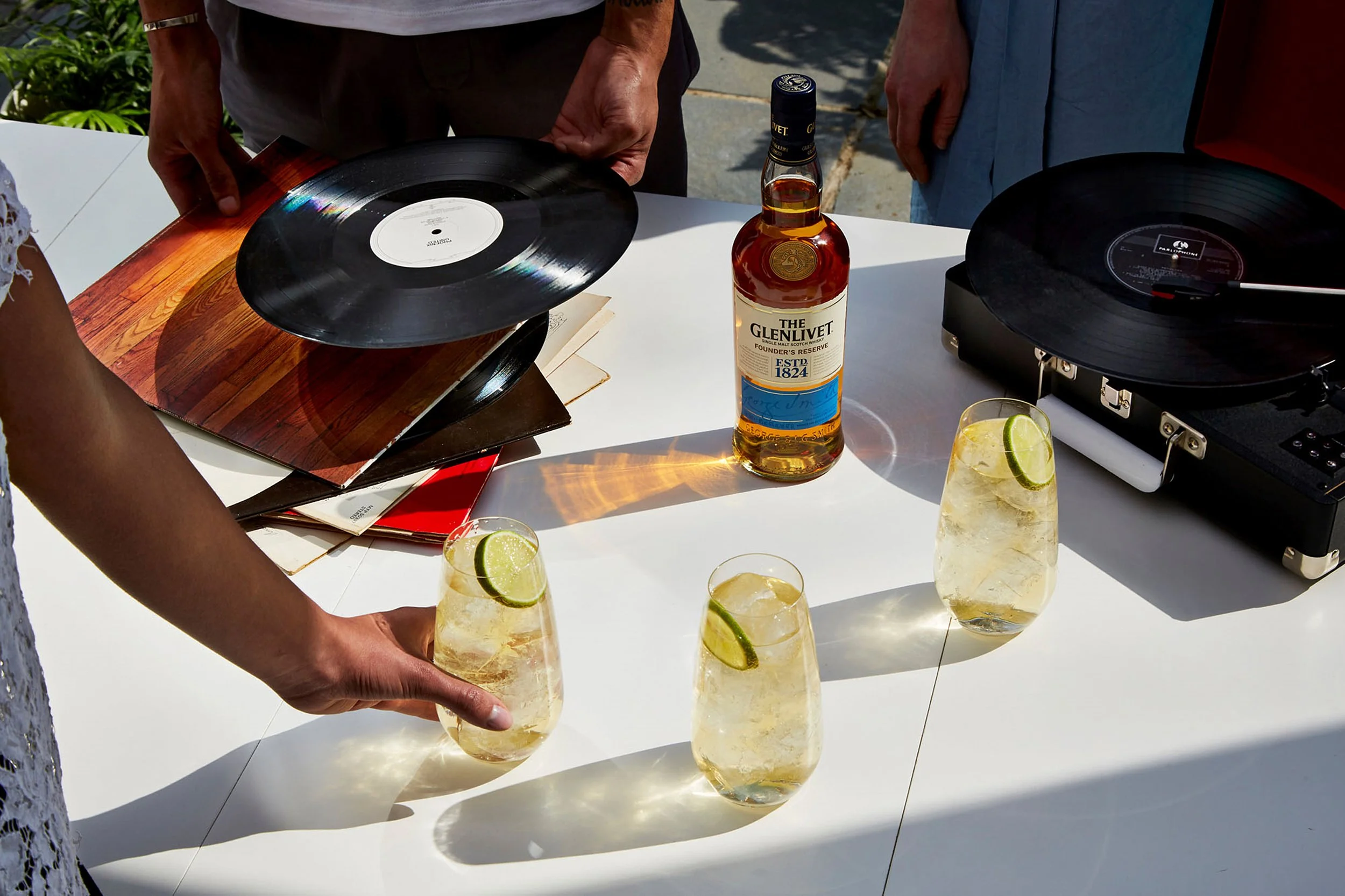 The Glenlivet whisky bottle and lime cocktails beside vinyl records and turntables on an outdoor table