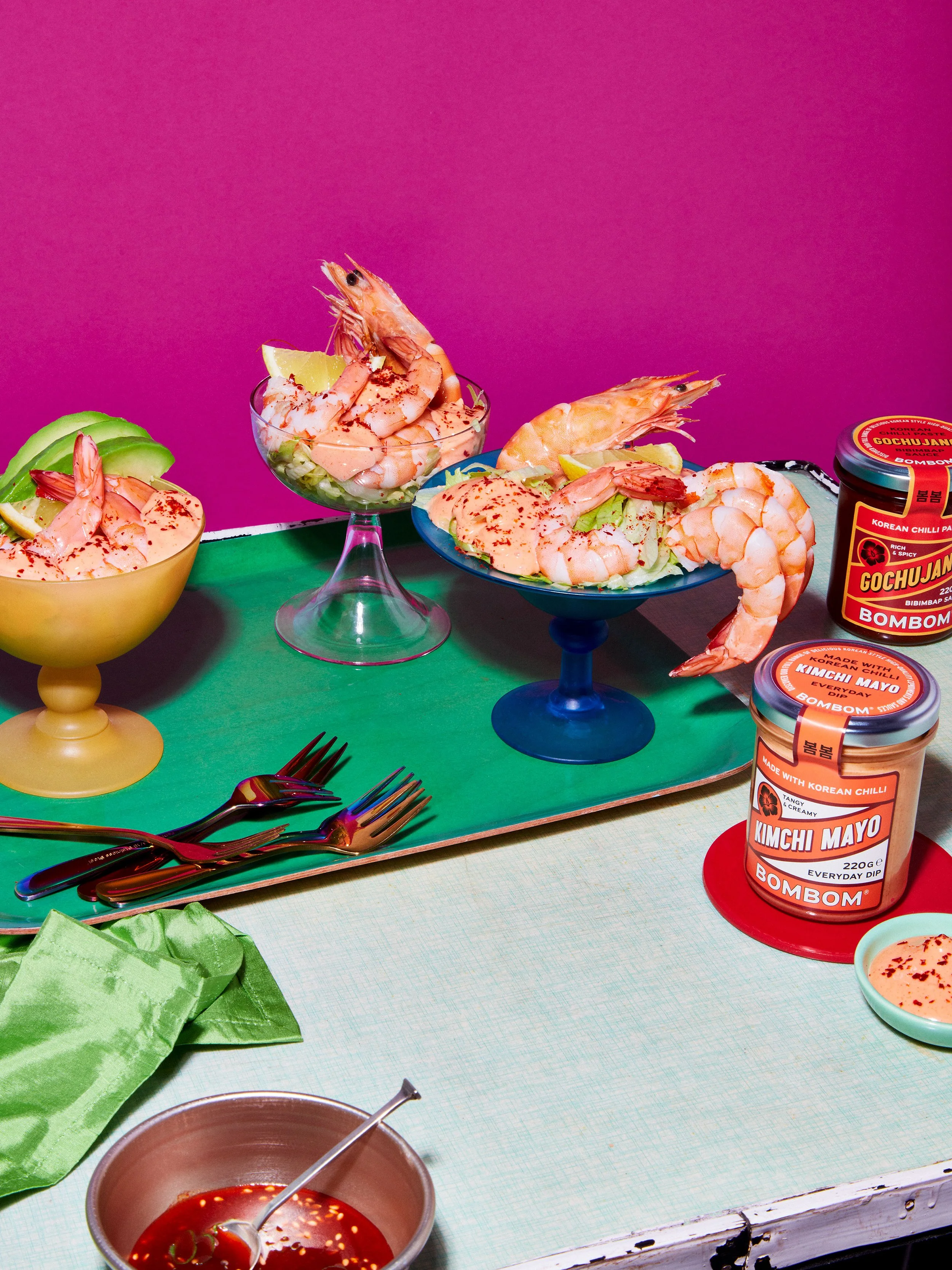 Shrimp cocktails and salads with creamy spicy sauce, lime wedges, and Korean gochujang and kimchi mayonnaise jars on a colorful table