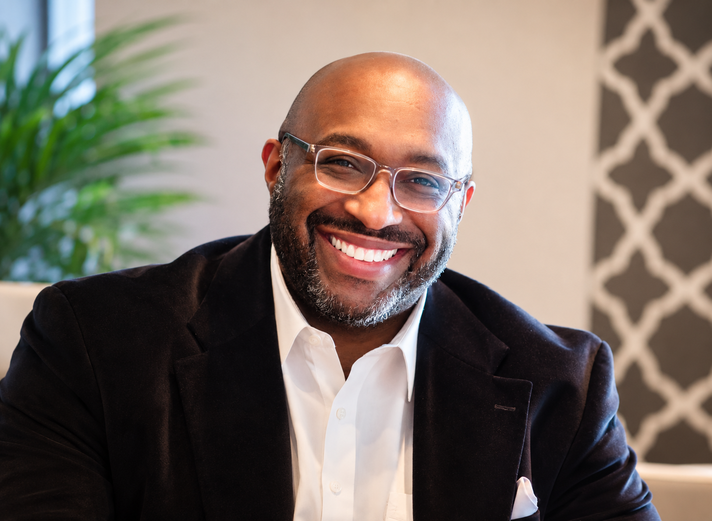 Smiling portrait of Bo Kemp wearing glasses, a black blazer, and a white shirt.