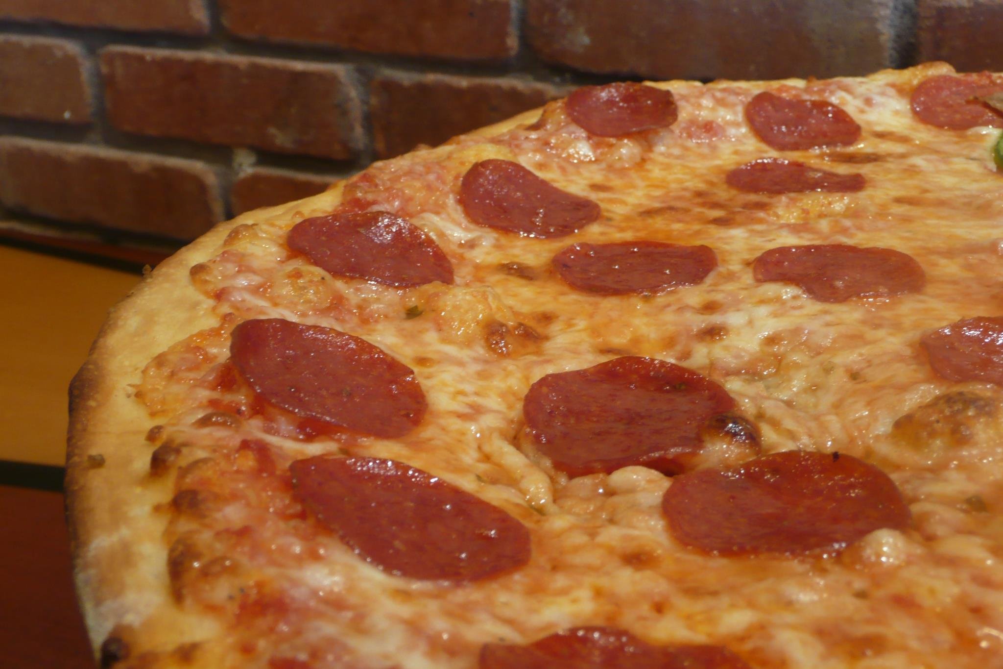 A close-up of a pepperoni pizza with melted cheese in front of a brick wall.