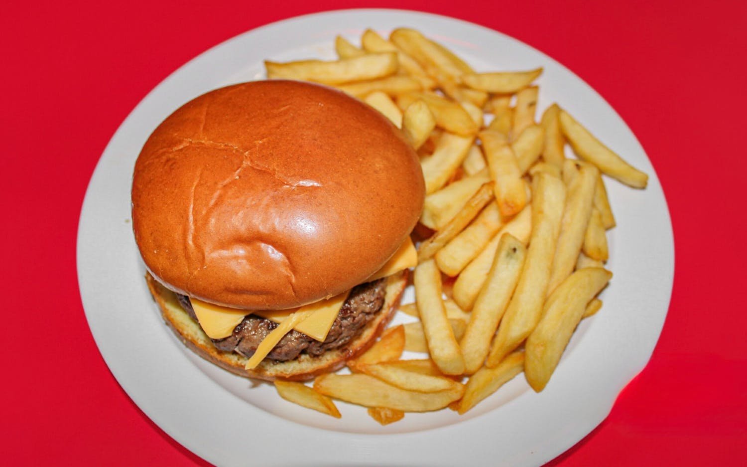 Plate with cheeseburger and French fries on a red background.