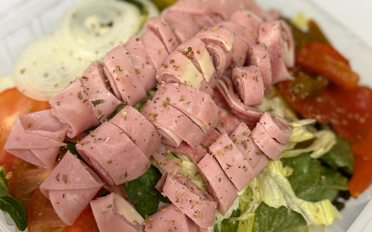 Salad with lettuce, tomato, cucumber, chopped onion, and sliced ham on top.