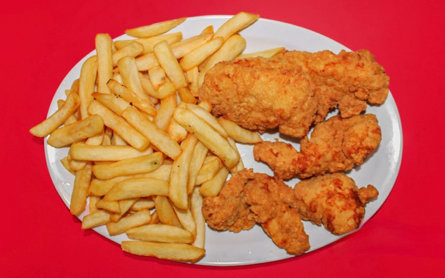 Plate with French fries and fried chicken drumsticks on a red surface.