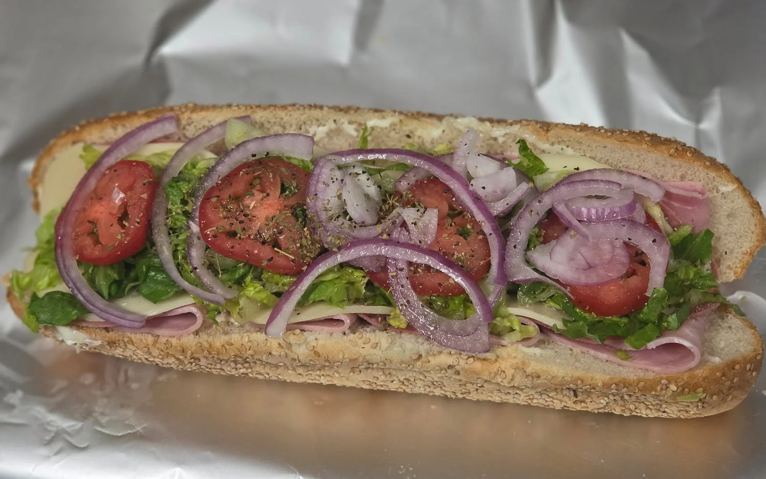A submarine sandwich with lettuce, tomato, onions, ham, and cheese on a sesame seed bun.