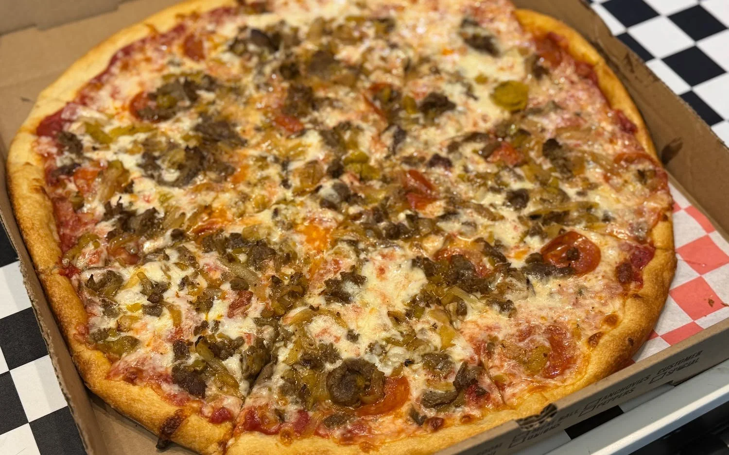 A pizza with cheese, pepperoni, beef, green peppers, and tomatoes in a cardboard box.