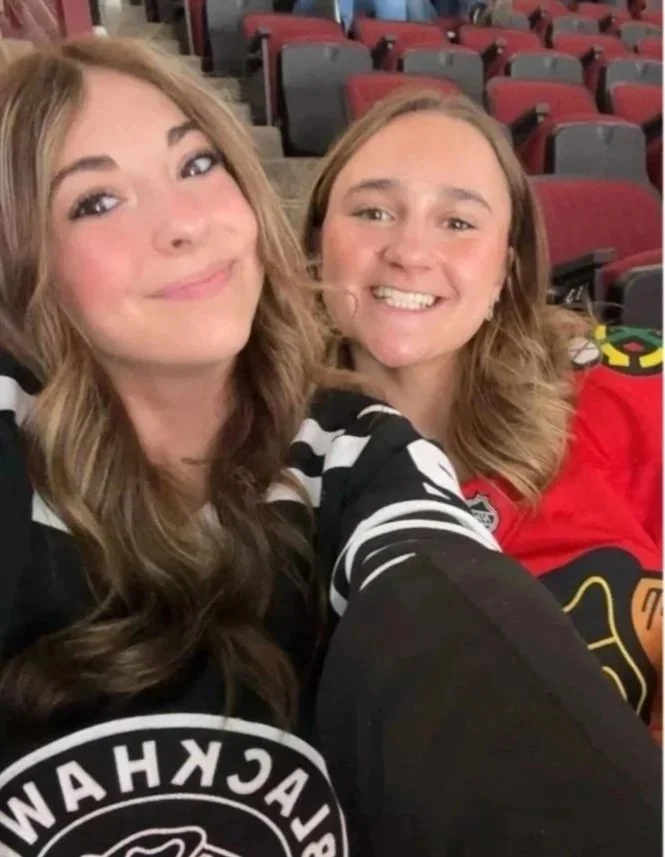Two women in sports jerseys taking a selfie in an empty arena with red seats.