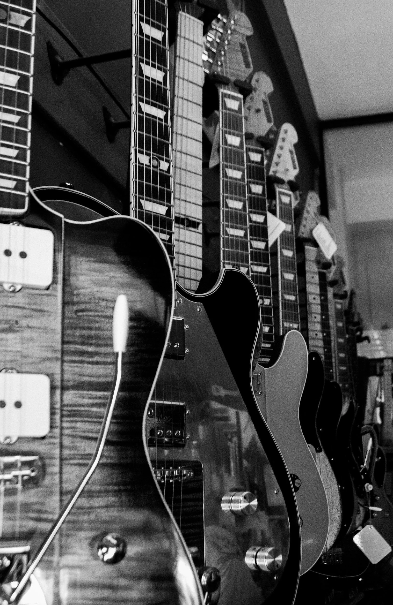 Multiple electric and acoustic guitars mounted on a wall, viewed at an angle in black and white.