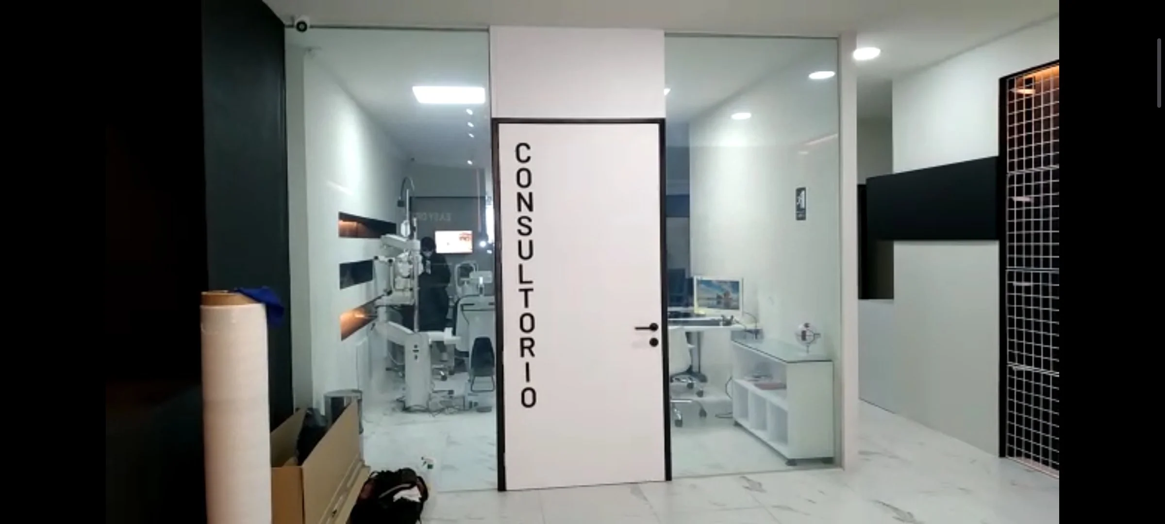 Smart Film claro en Entrada a un consultorio con cartel que dice 'CONSULTORIO', vista del interior con equipo médico y personal trabajando.
