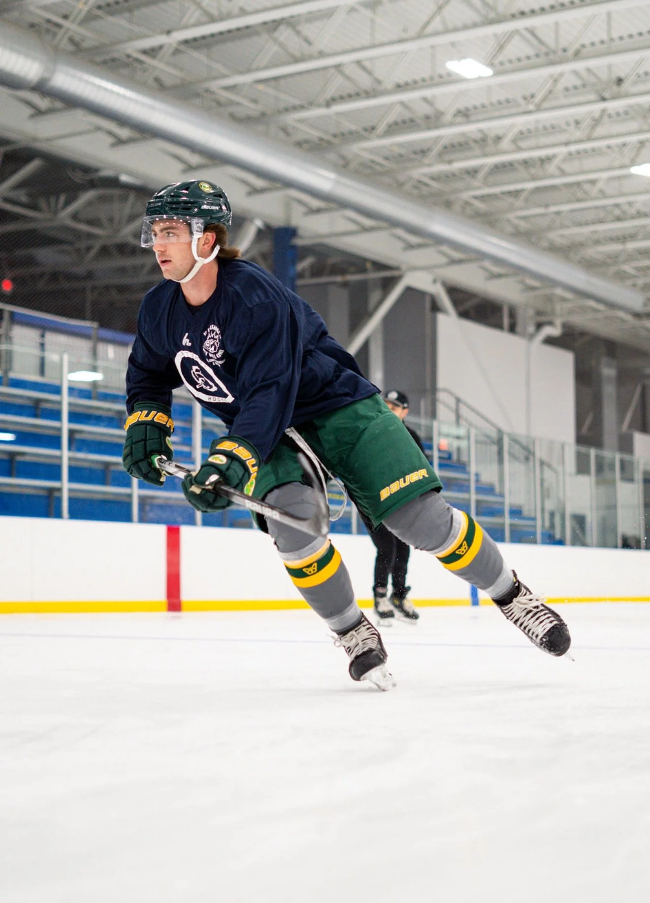 A hockey player wearing a helmet, navy blue jersey, and green shorts on the ice rink during a game or practice.