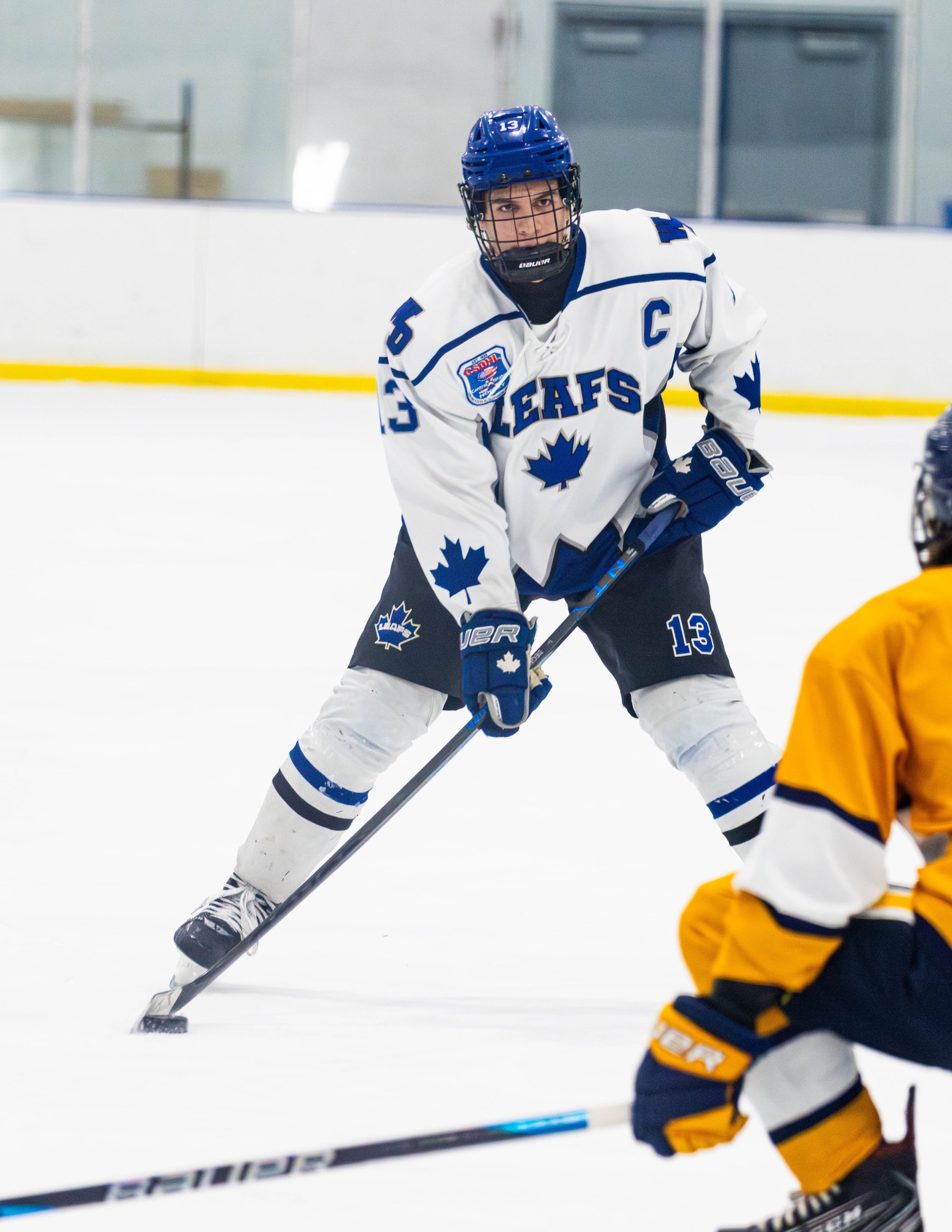 Ice hockey player in a Toronto Maple Leafs uniform leaning forward on the ice during a game.