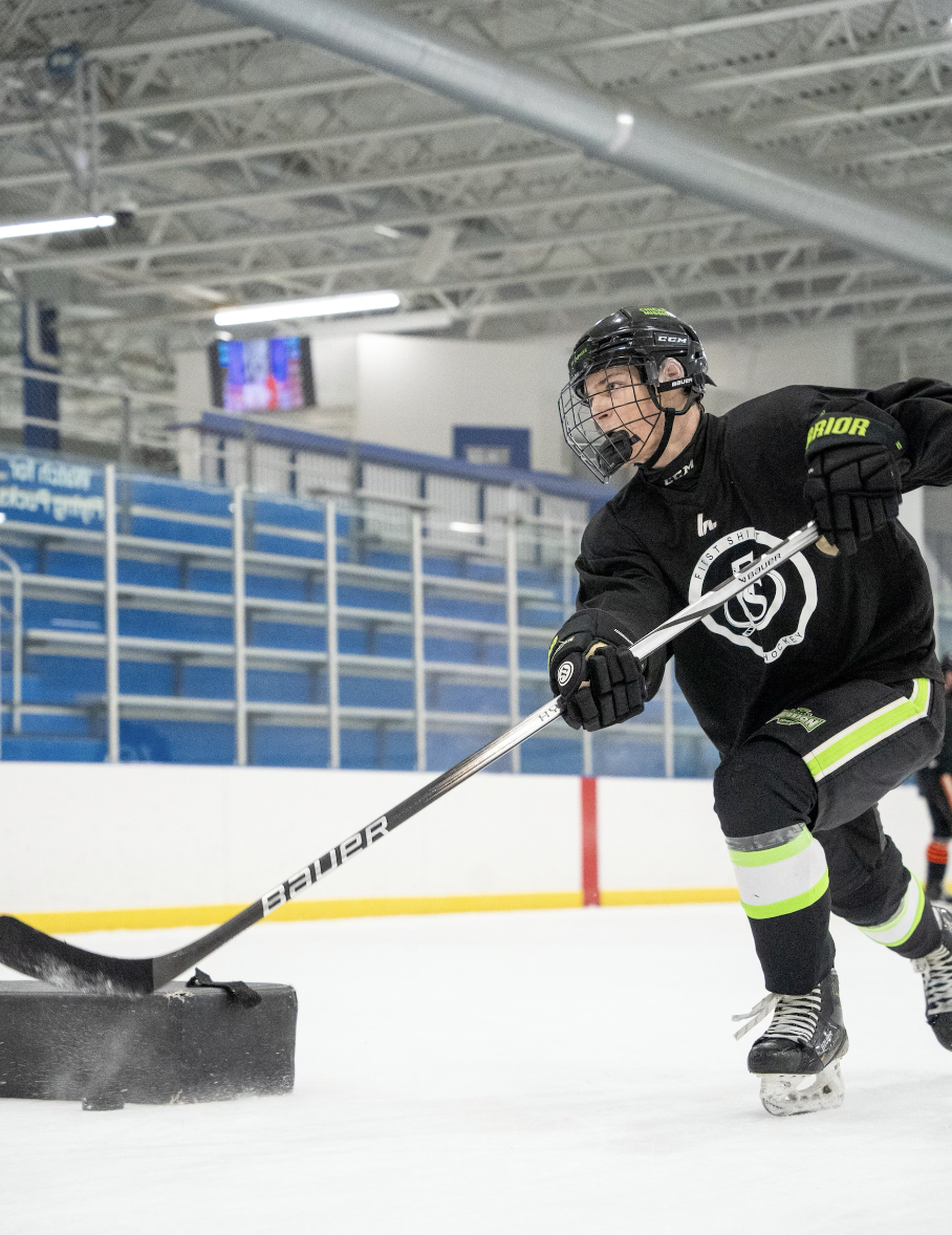Hockey player in black uniform and helmet practicing skills on an indoor ice rink.