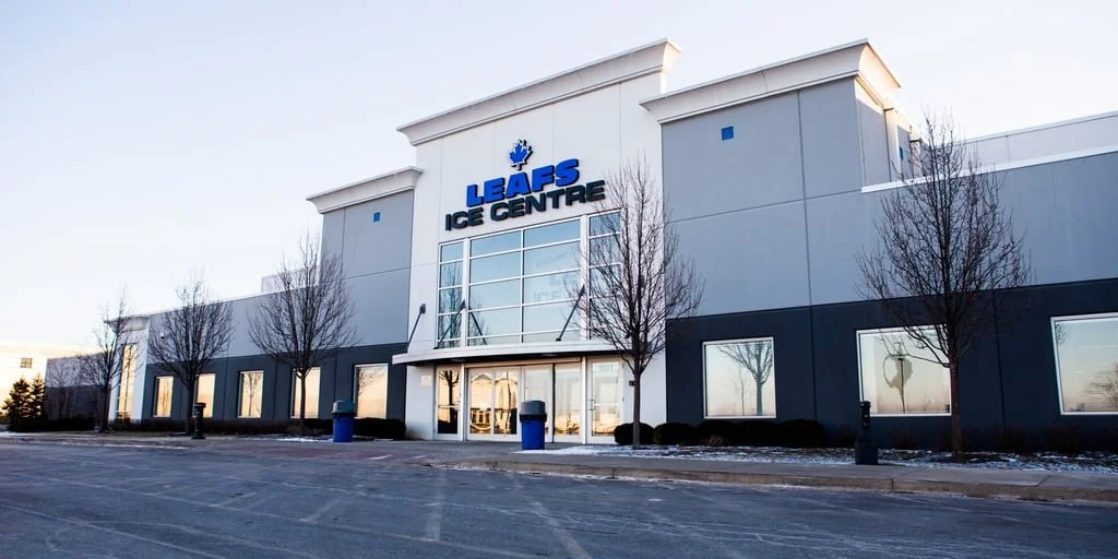 Exterior of Leafs Ice Centre with leaf logo and blue and gray building, leafless trees in front, snow on the ground.