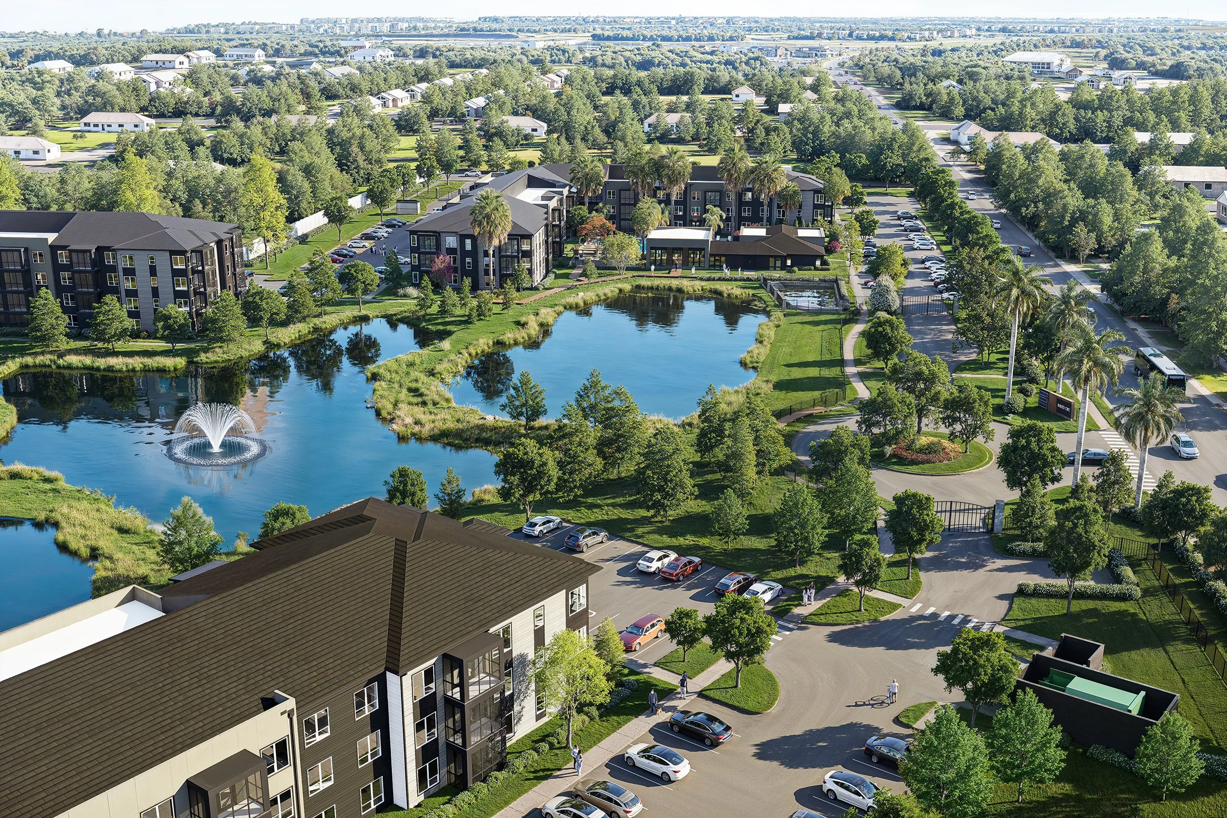 An aerial view of a residential neighborhood with multiple apartment buildings, a pond with a fountain, trees, parking lots, and roads.