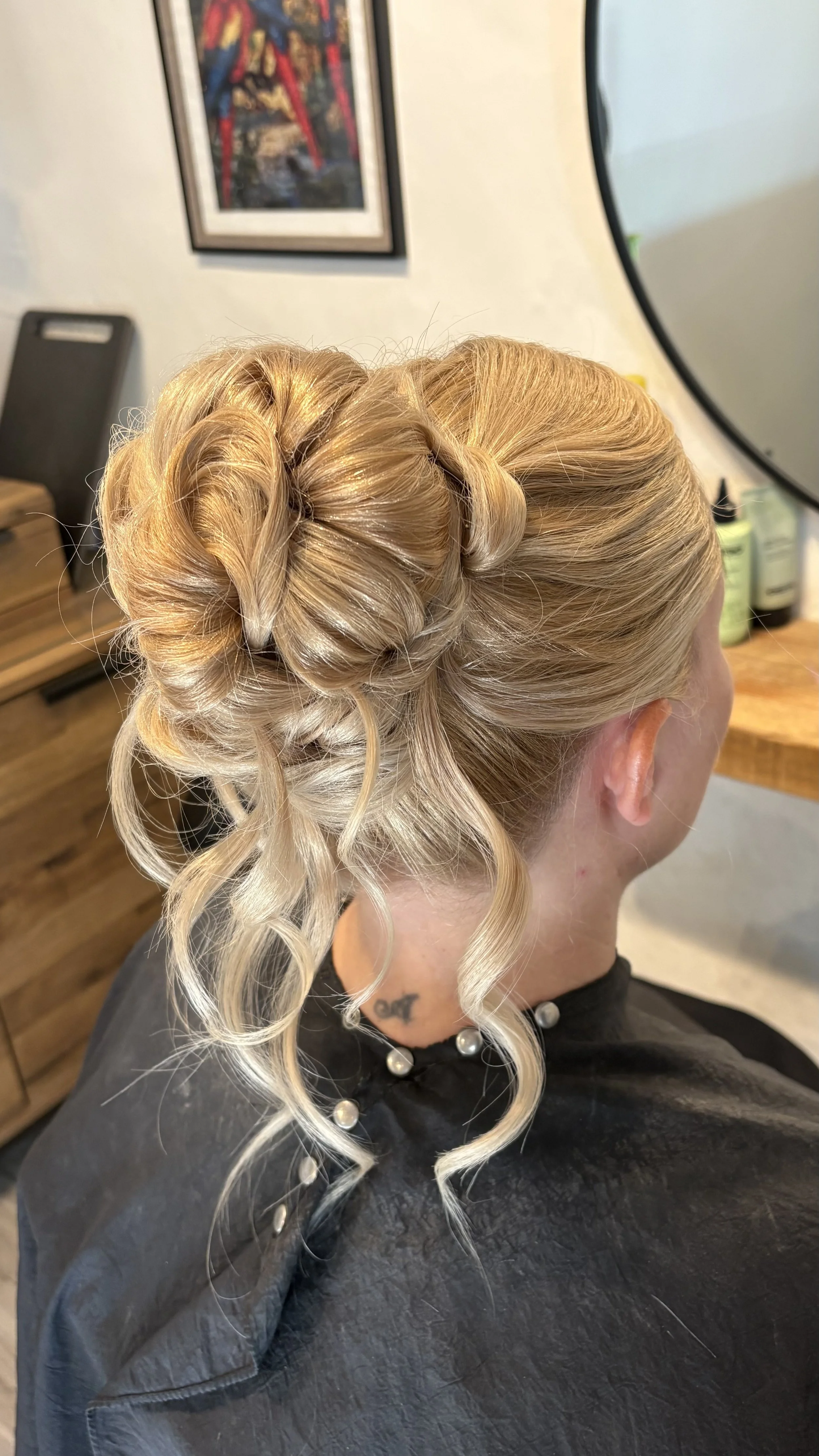 Woman with blonde hair styled in an elegant updo with curls, sitting in a salon chair.