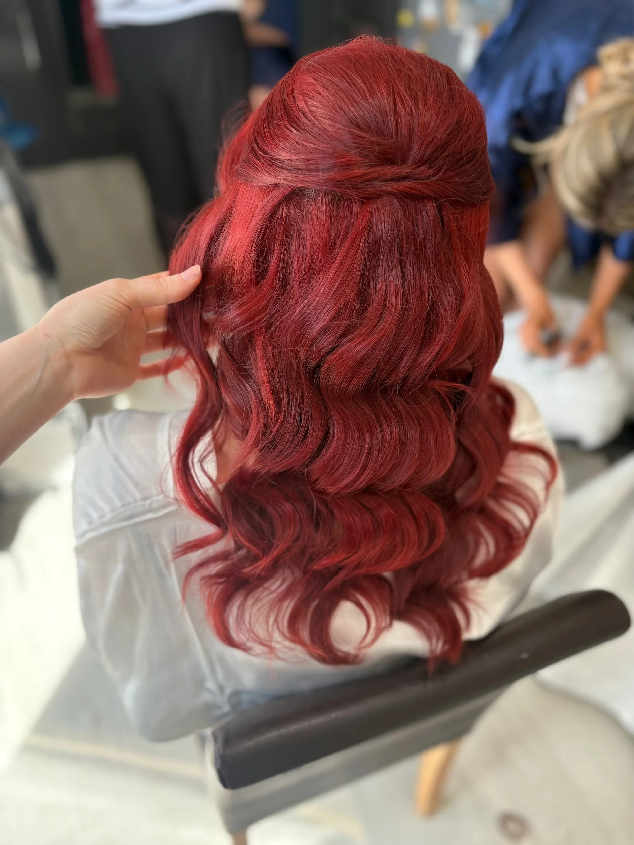 Close-up of a person with long, wavy red hair being styled or checked in a salon setting.