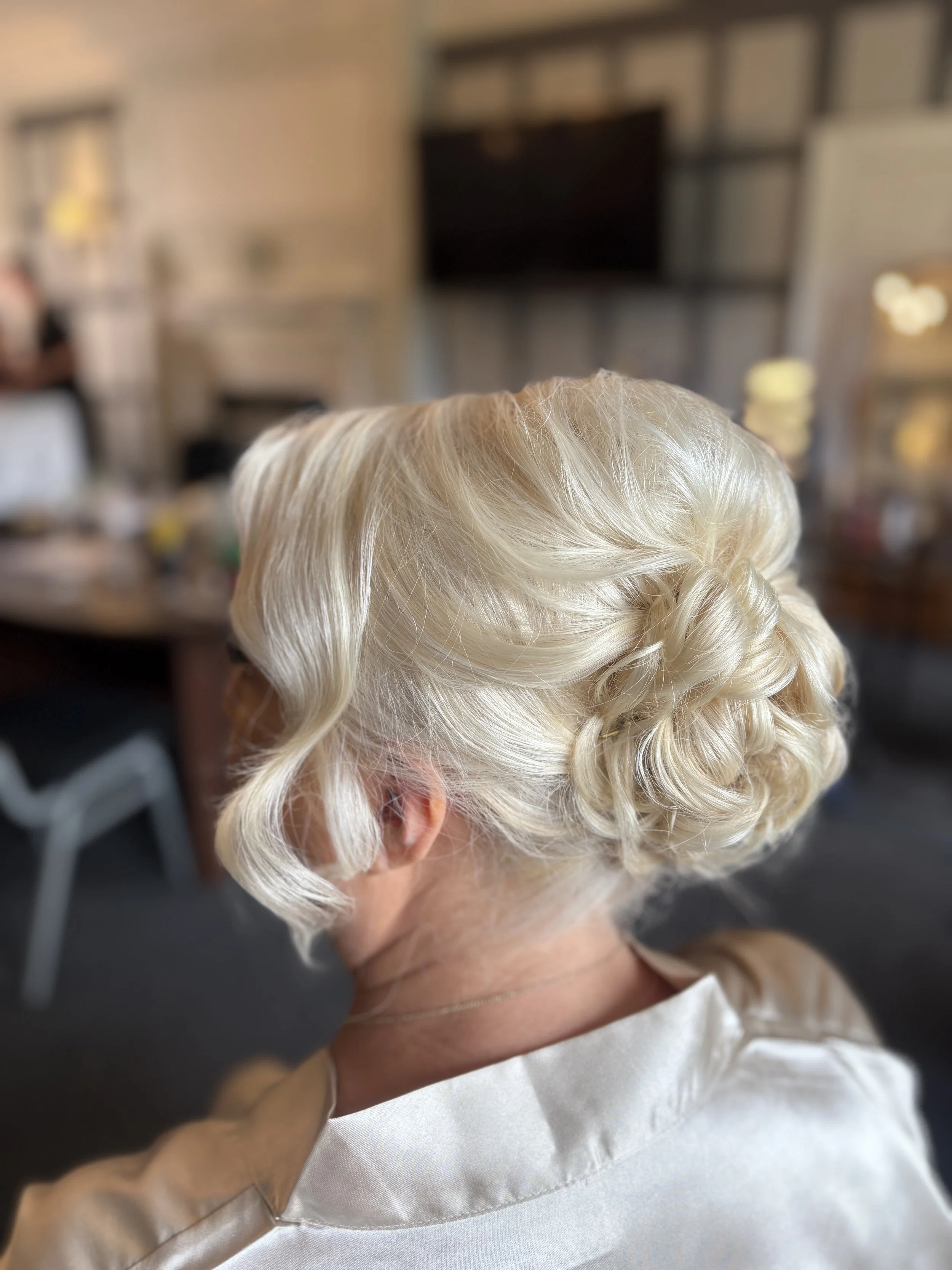 Close-up of a woman with platinum blonde, vintage-style curls, getting her hair styled in a salon.