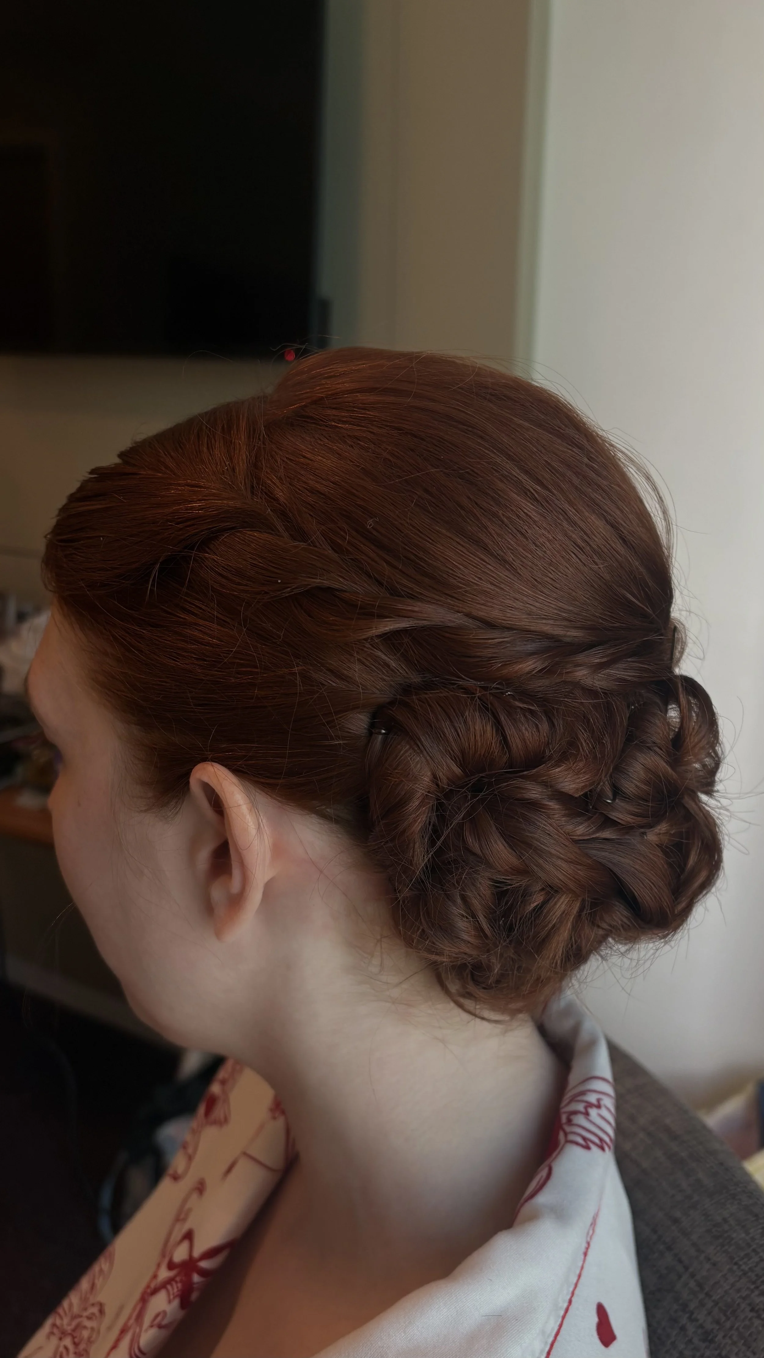 A woman's head with styled auburn hair, featuring a twisted crown and a curled bun at the back.