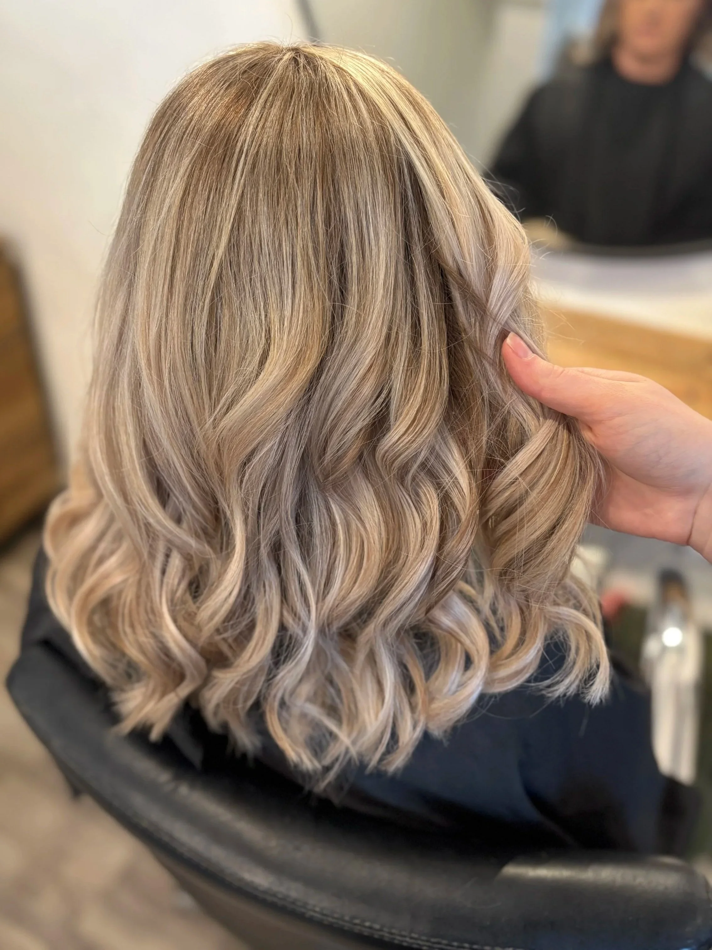 Close-up of blonde, wavy hair on a person's head, with someone hand gently touching the hair.