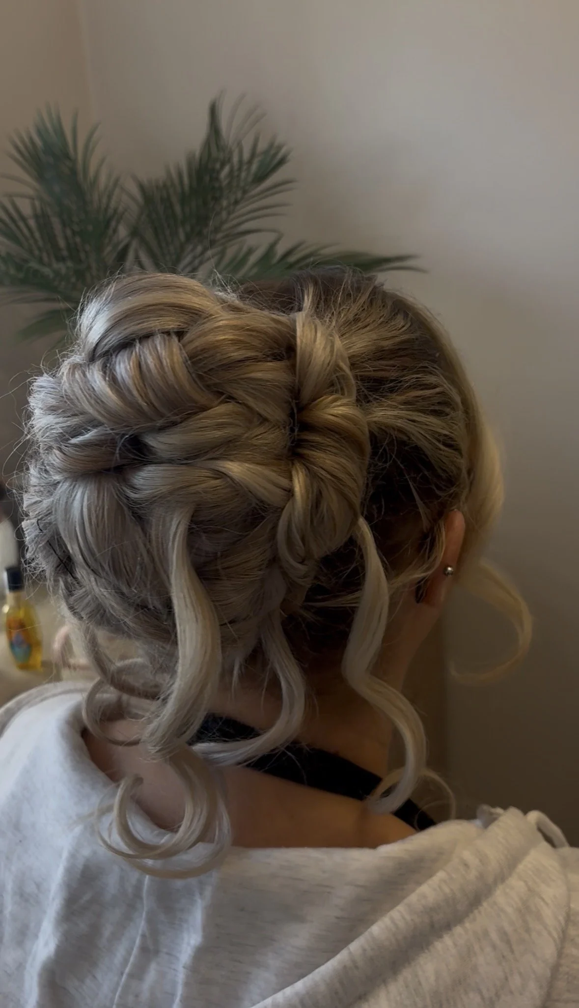 A woman with blonde hair styled in an intricate braid updo with loose curls at the ends.