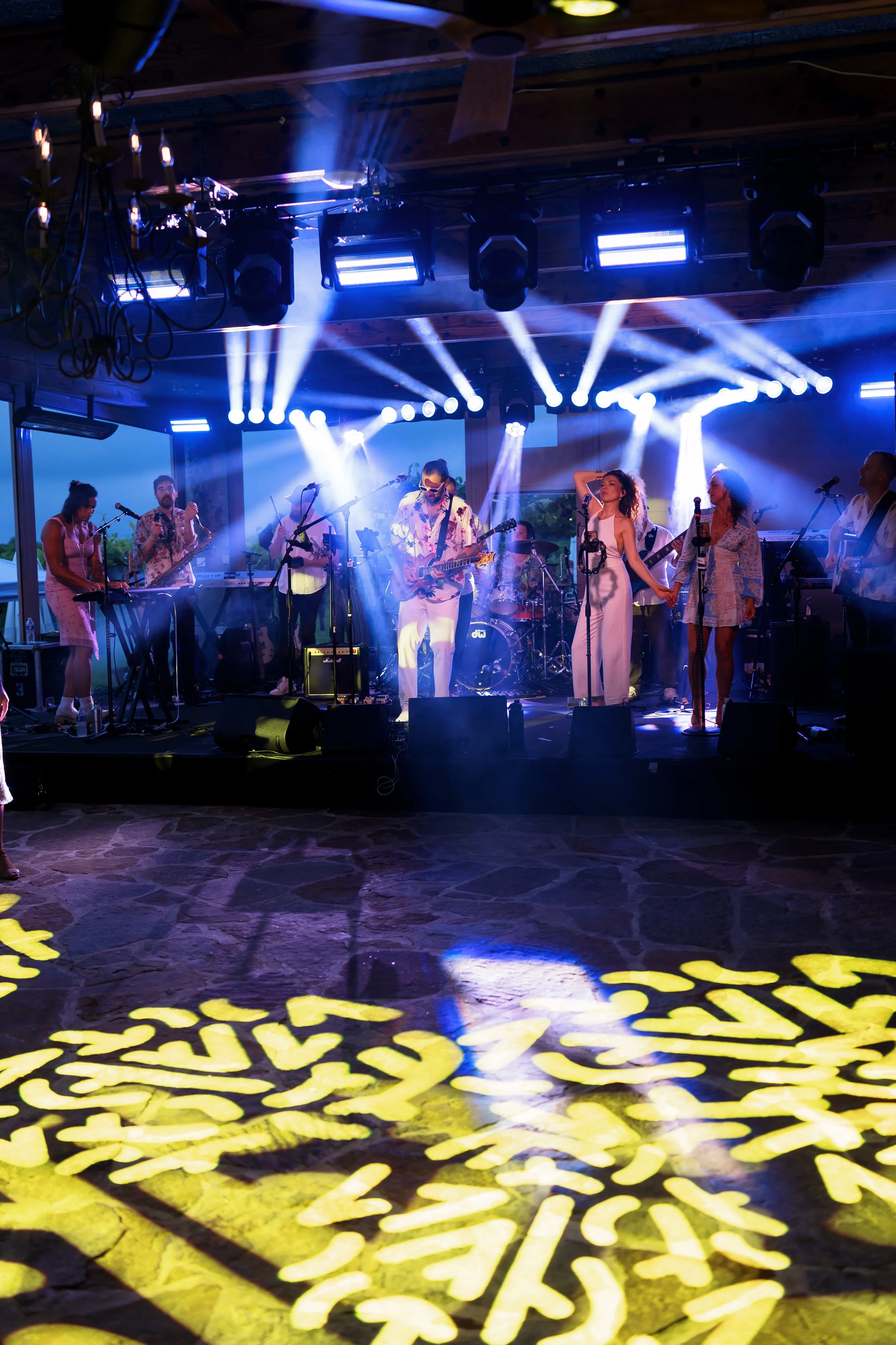 Live band performing on a stage with blue spotlights, musicians, singers, and colorful floor lighting