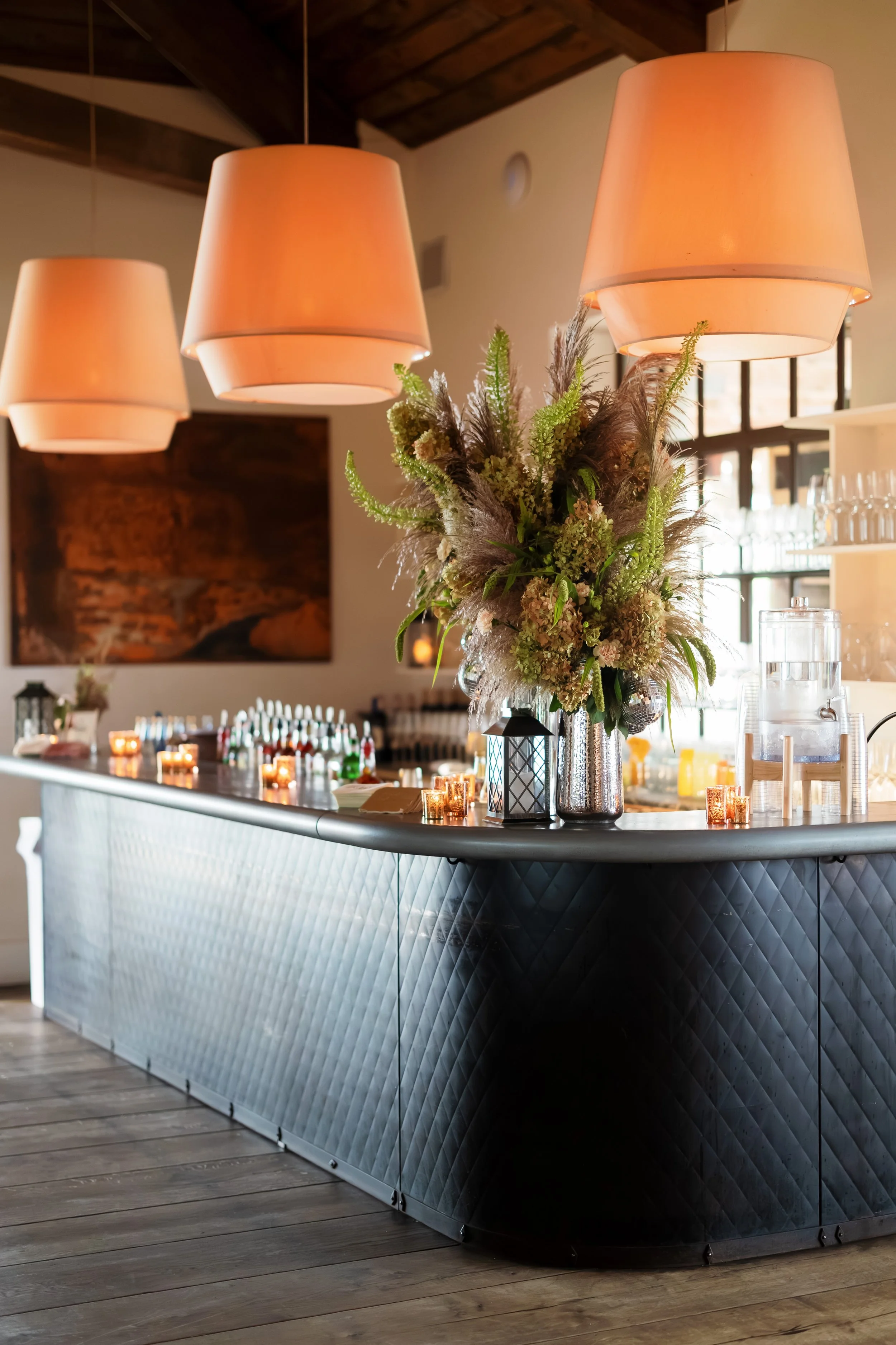 Elegant restaurant or bar interior with glowing pendant lights, floral centerpiece, candles, and a quilted black-and-white bar.