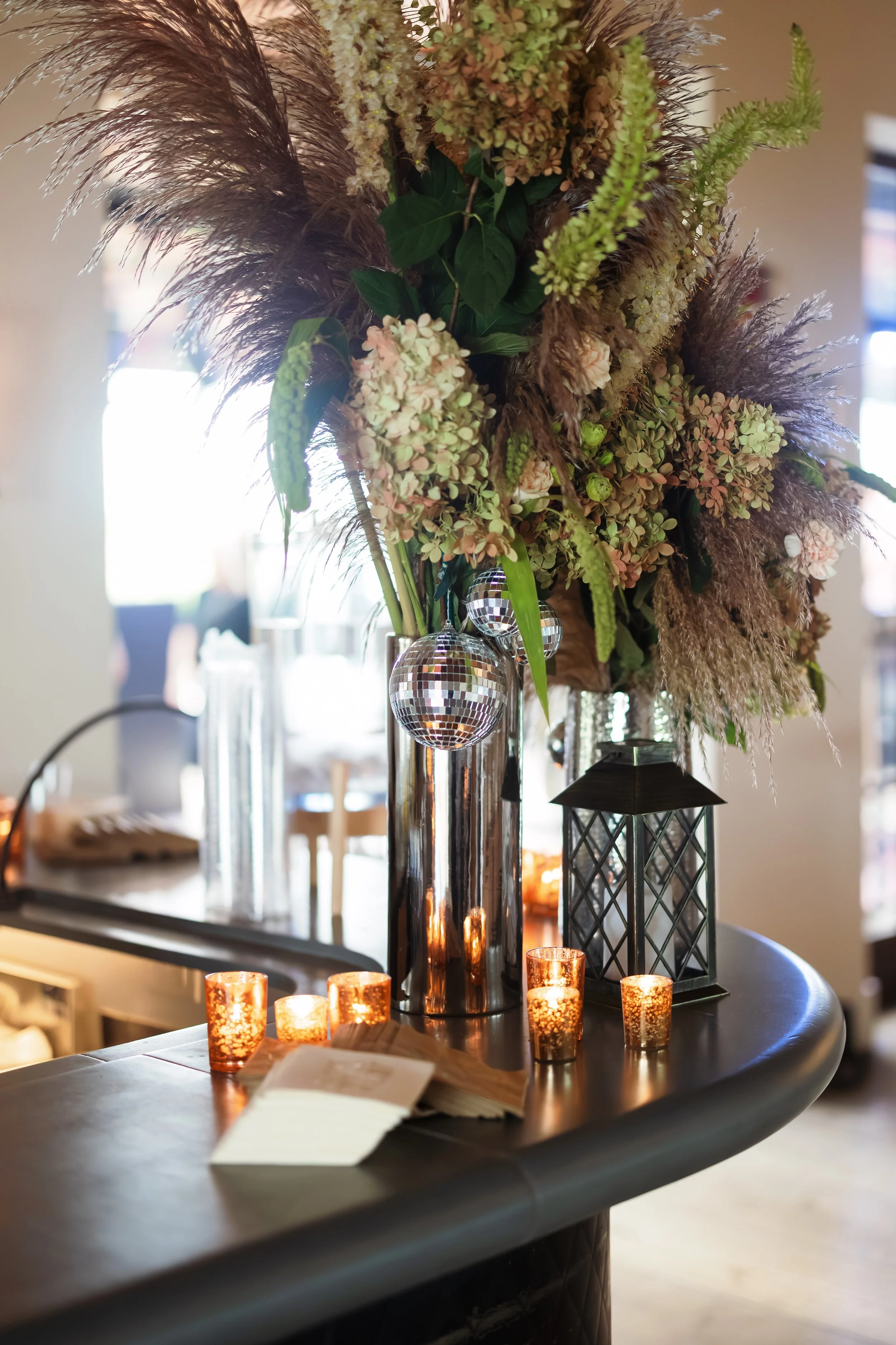 Elegant floral arrangement with pampas grass, hydrangeas, greenery, disco balls, and glowing candles on a table