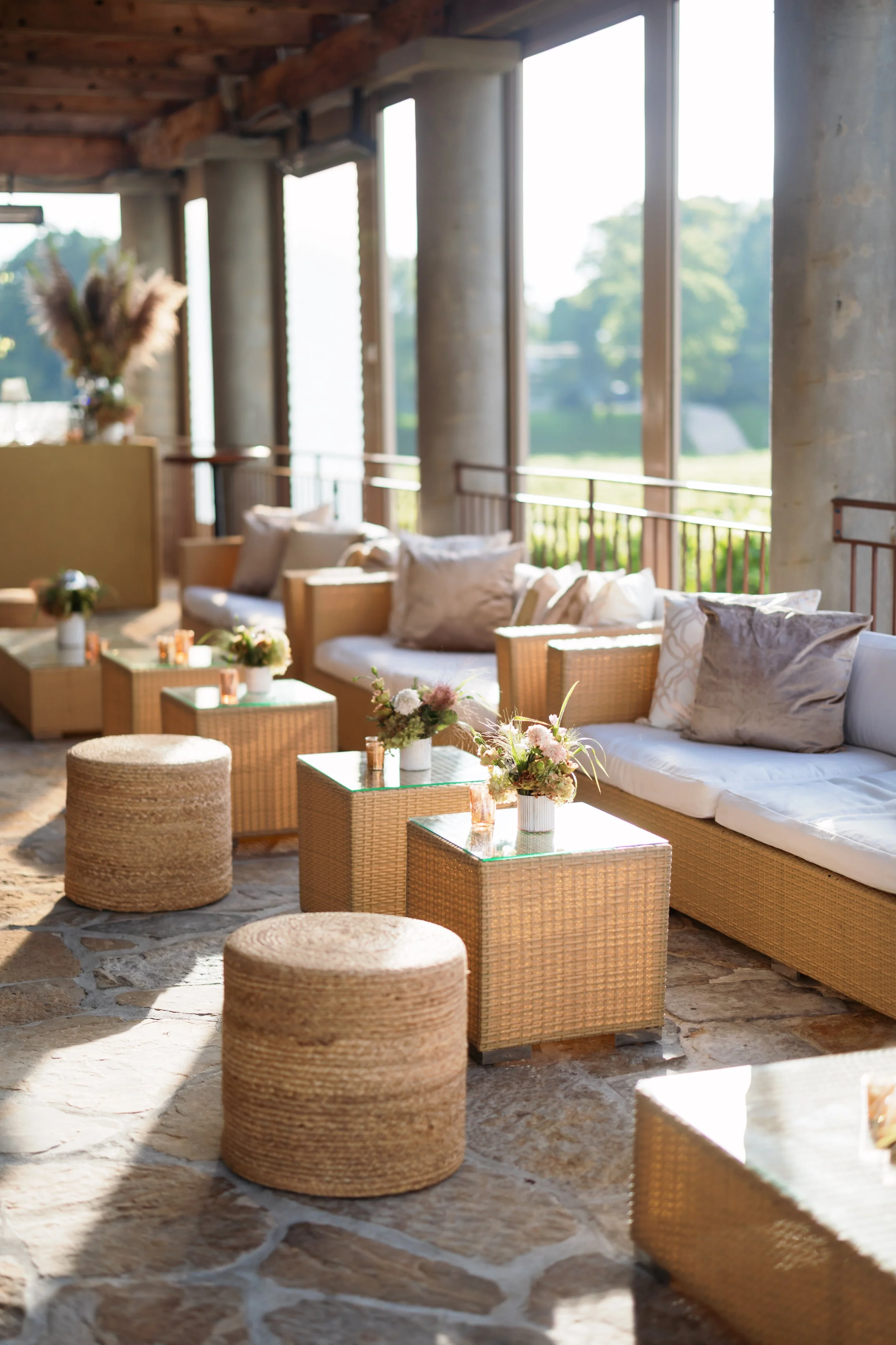 Bright rustic sunroom with wicker sofas, glass coffee tables, floral arrangements, and large windows overlooking greenery