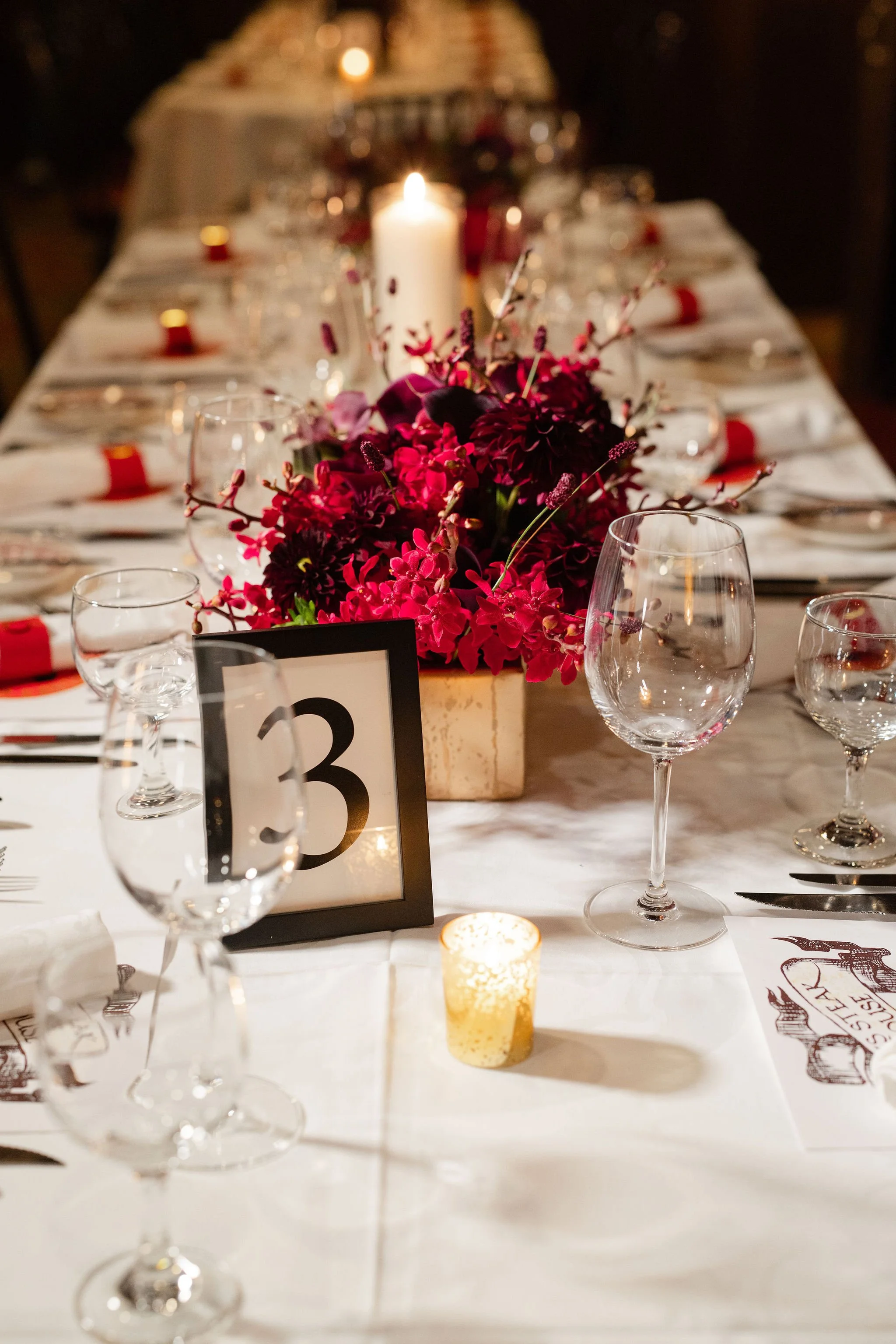 Elegant banquet table with red floral centerpiece, glowing candles, wine glasses, and a table number 3