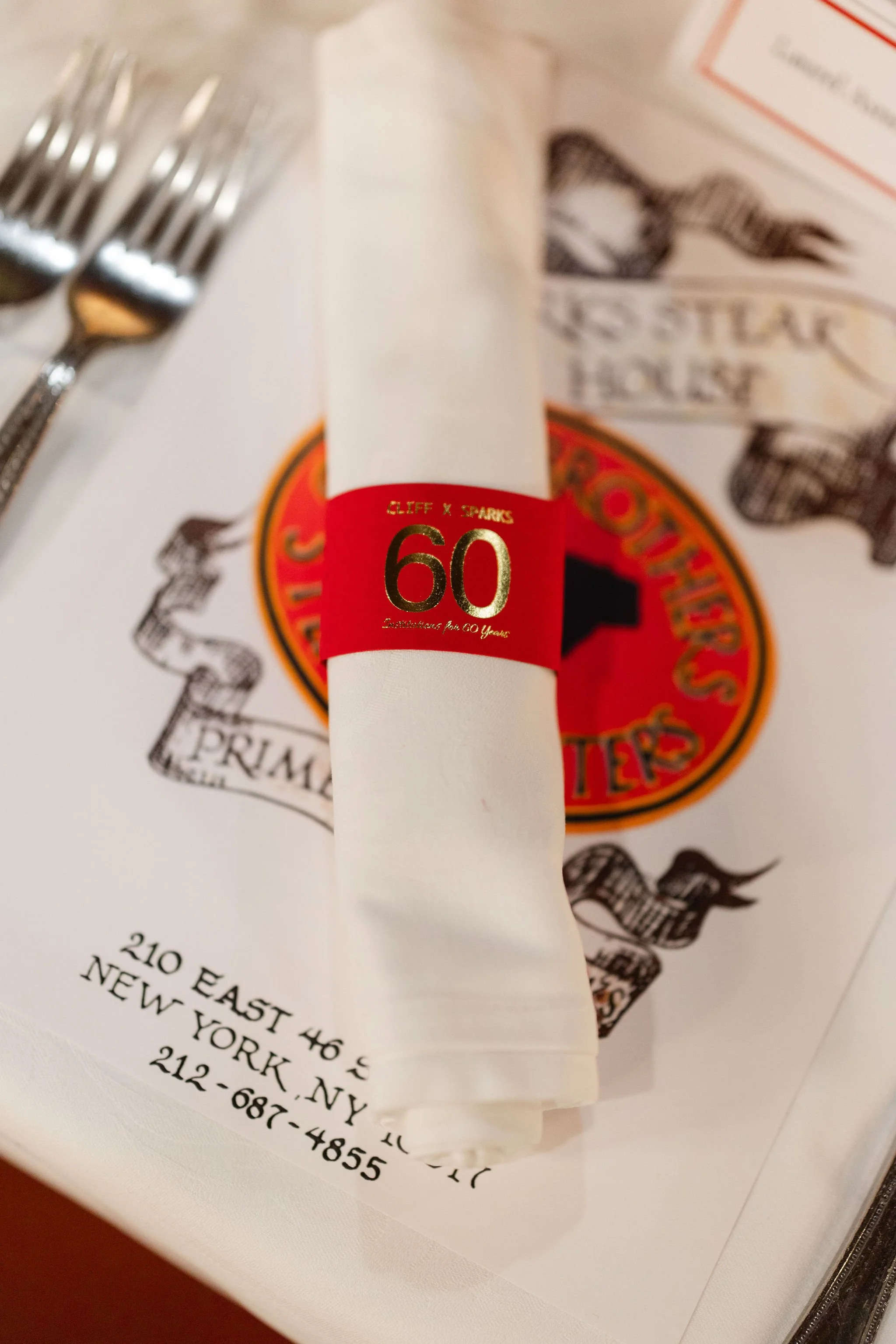 Close-up of a wedding invitation, white napkin, silverware, decorative red and gold plate, and printed menu on a table