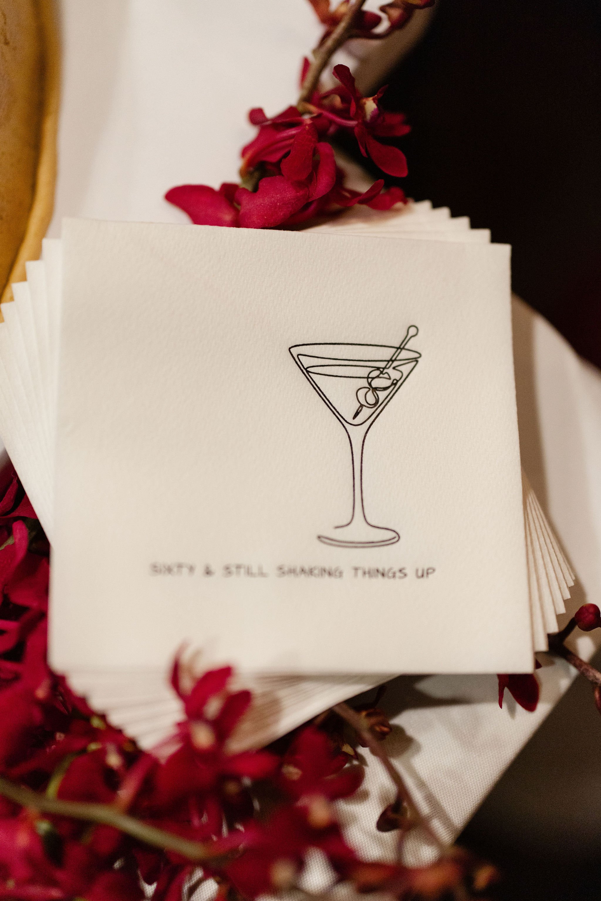 Stack of cocktail napkins featuring a martini glass illustration and the phrase “Sip, sip, hooray,” surrounded by red flowers.