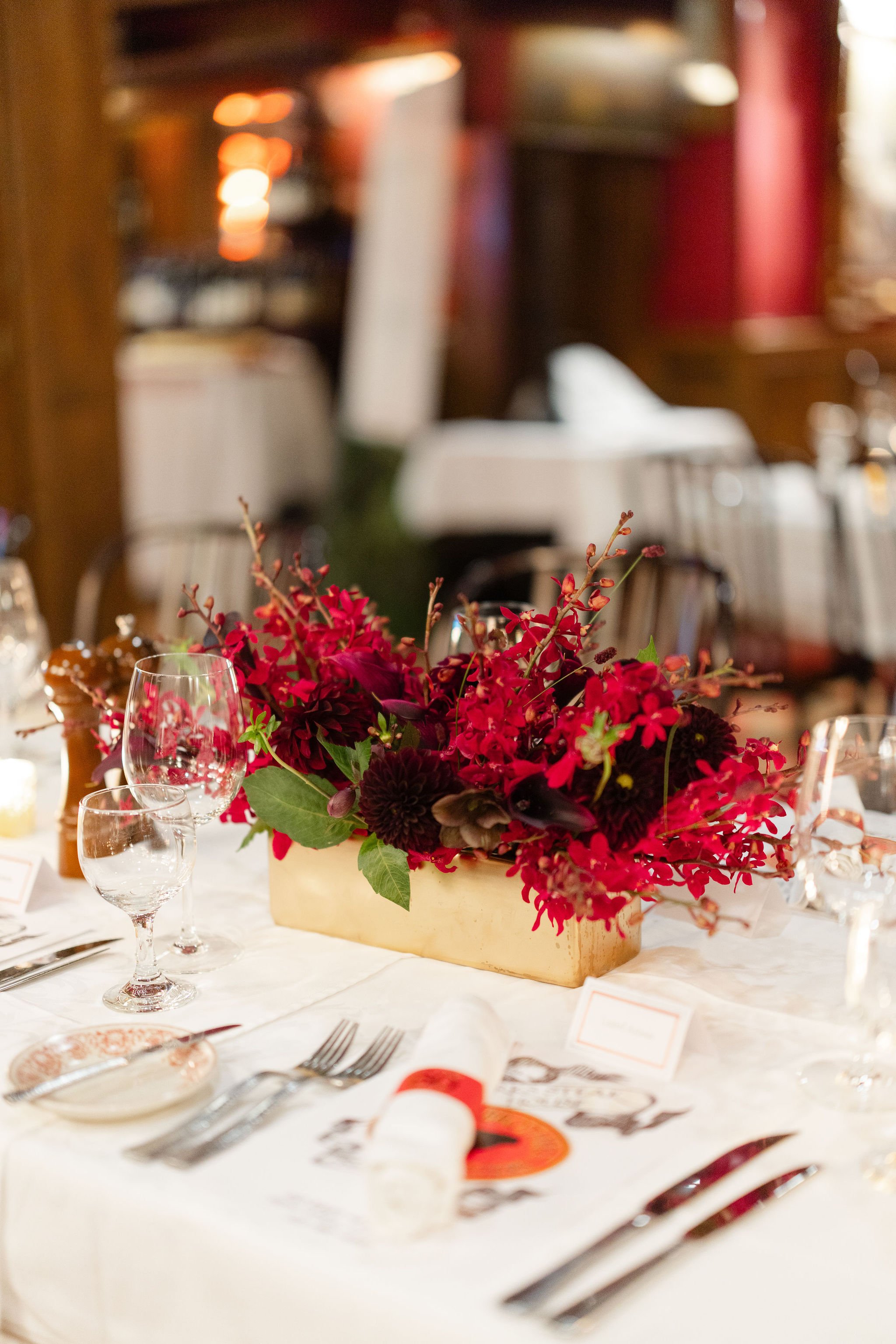 Elegant dining table with a vivid red floral centerpiece, wine glasses, place settings, and softly blurred restaurant décor