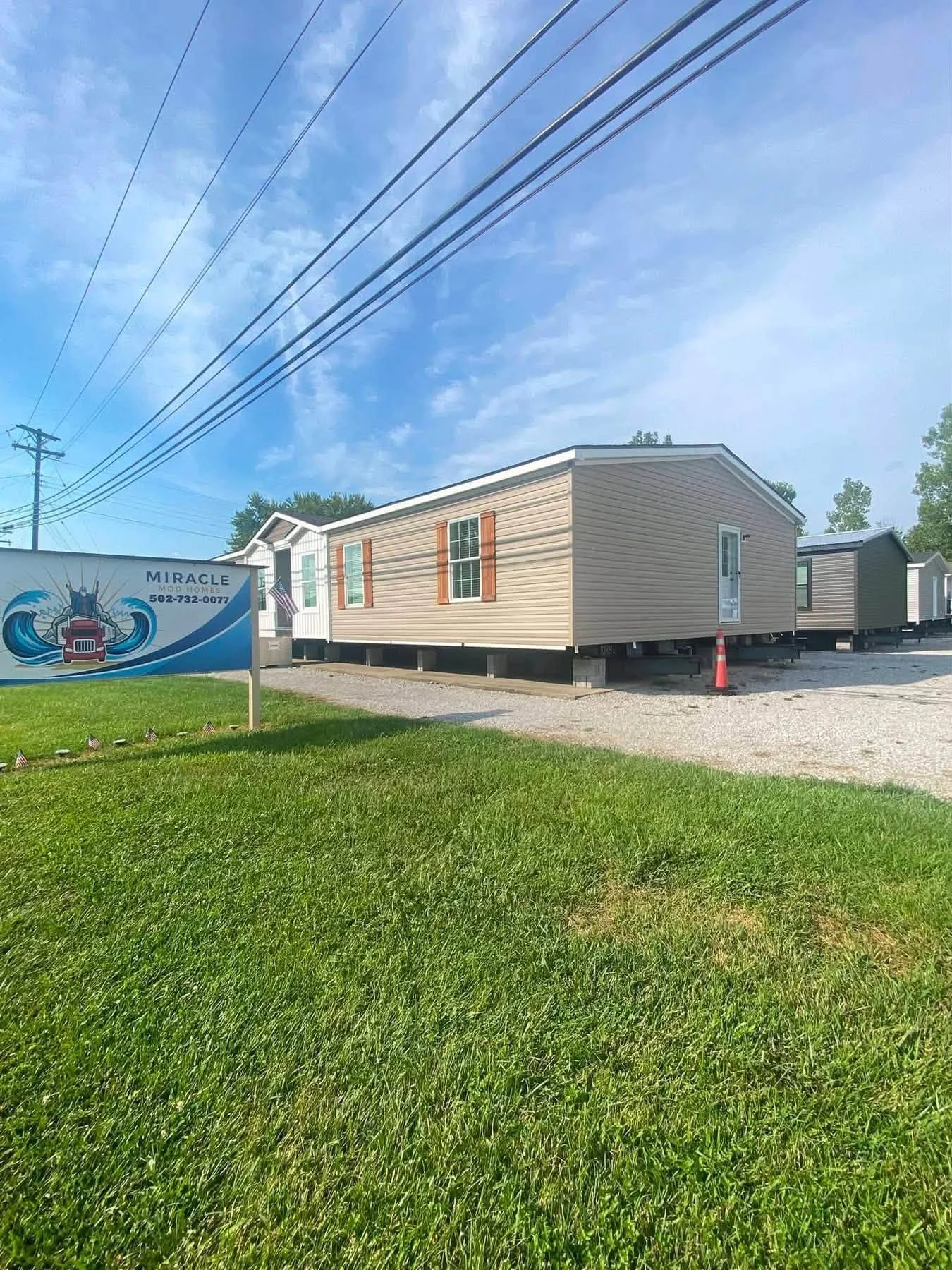 Manufactured homes for sale at Miracle Mobile Homes, displayed on a grassy lot beneath overhead power lines.