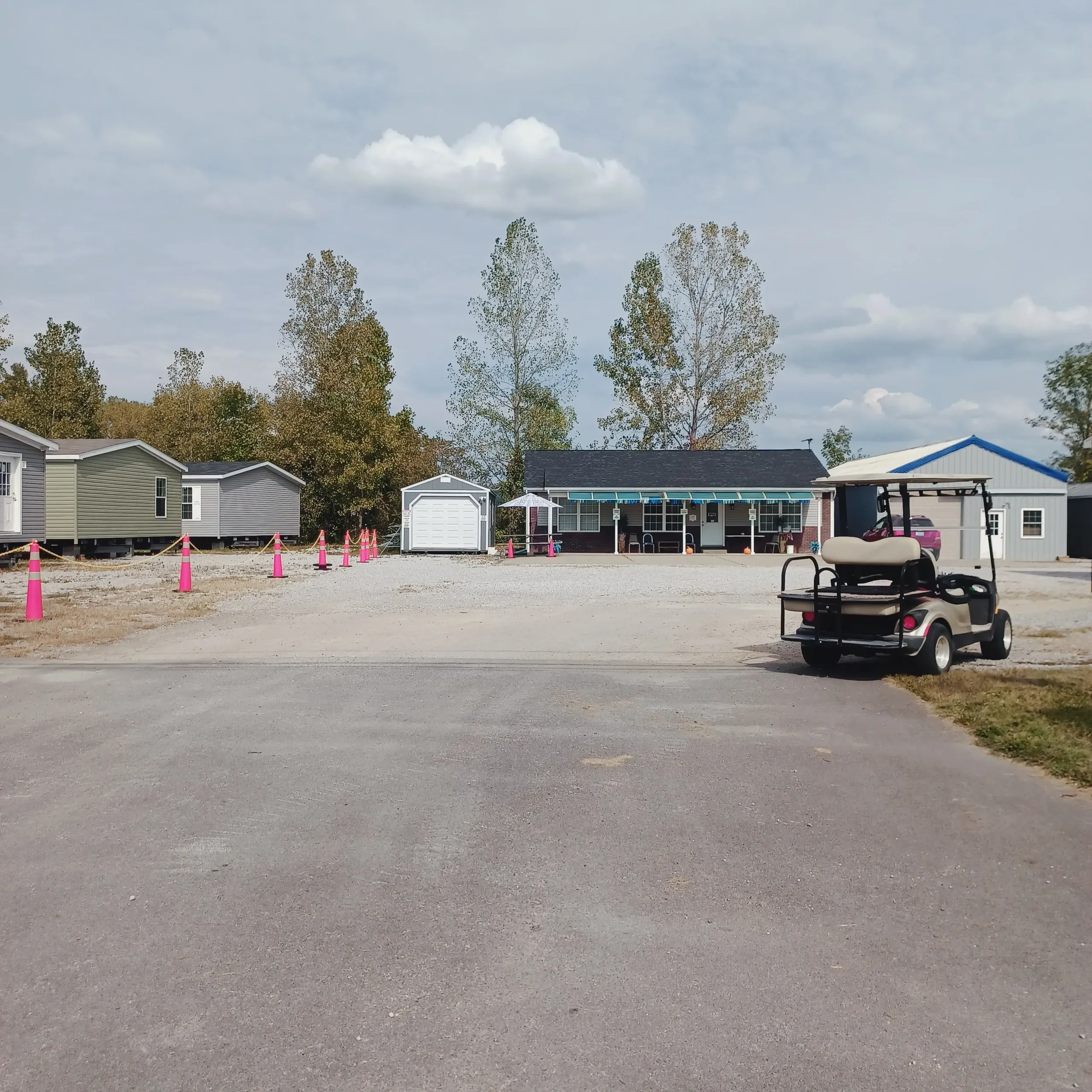 Golf cart parked in front of mobile homes and a community office under a cloudy sky