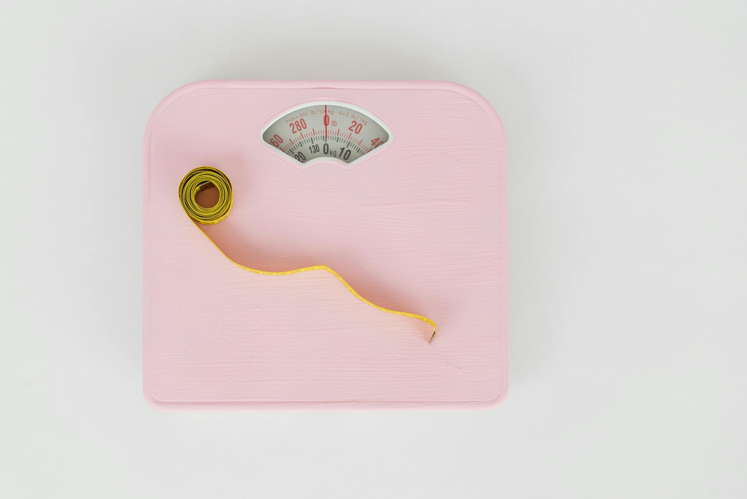 Pink bathroom scale with a yellow measuring tape coiled on top