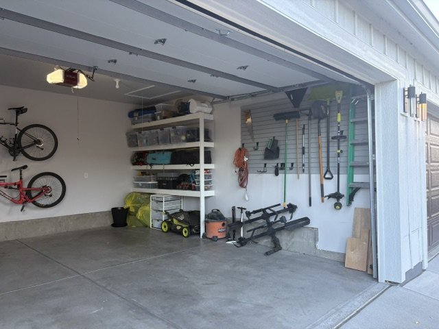 Organized residential garage with bicycles, shelving, lawn equipment, hand tools, and workout equipment