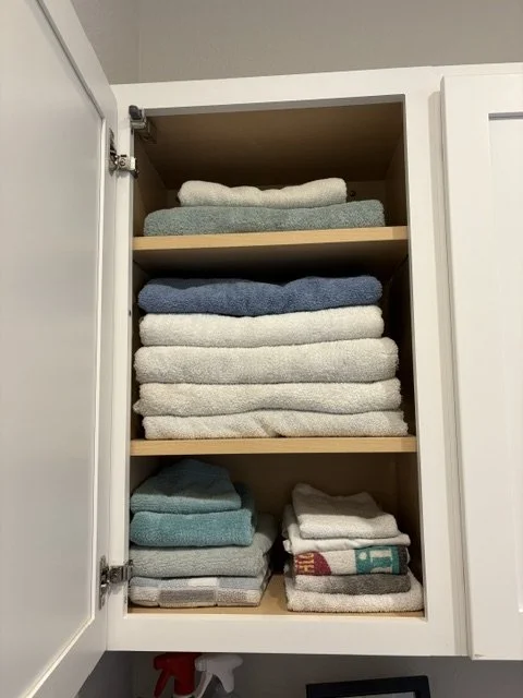 Open bathroom cabinet neatly stacked with folded white, blue, and teal towels on wooden shelves