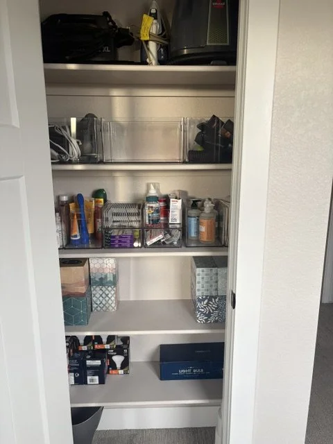 Organized household storage closet with electronics, cleaning supplies, toiletries, baskets, and miscellaneous items on shelves