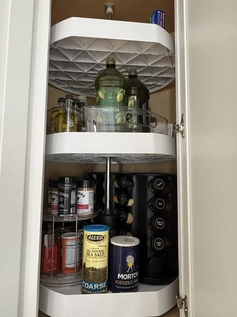 Open corner kitchen cabinet organizer stocked with olive oil, spices, sea salt, and other seasonings