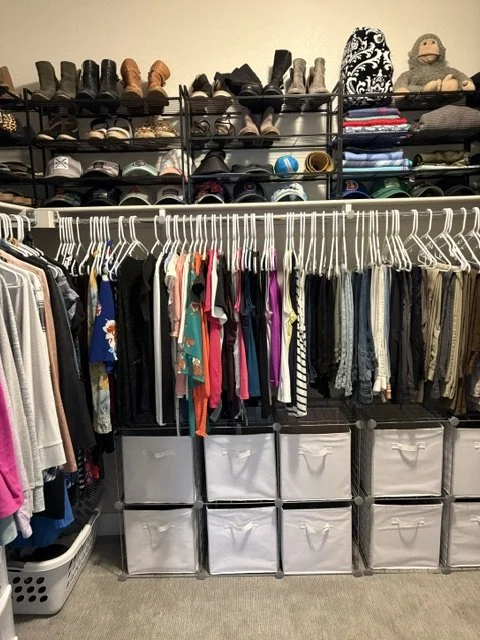 Organized walk-in closet with shoes, hats, folded clothes, hanging garments, fabric storage bins, and laundry baskets.